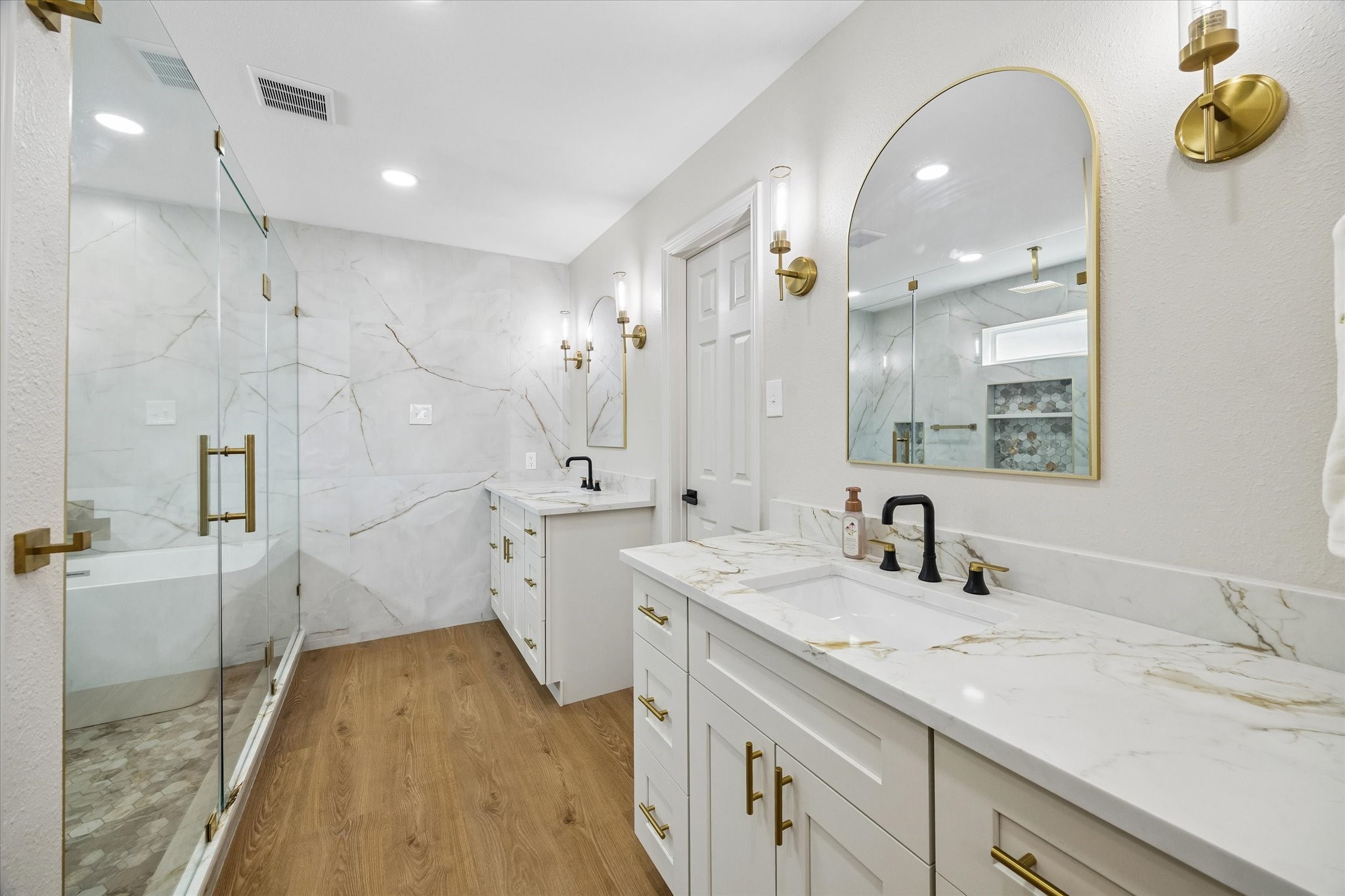 Elegant bathroom featuring a spacious glass-enclosed shower, luxurious quartz countertops, and stylish gold fixtures, all complemented by warm wood looking flooring.