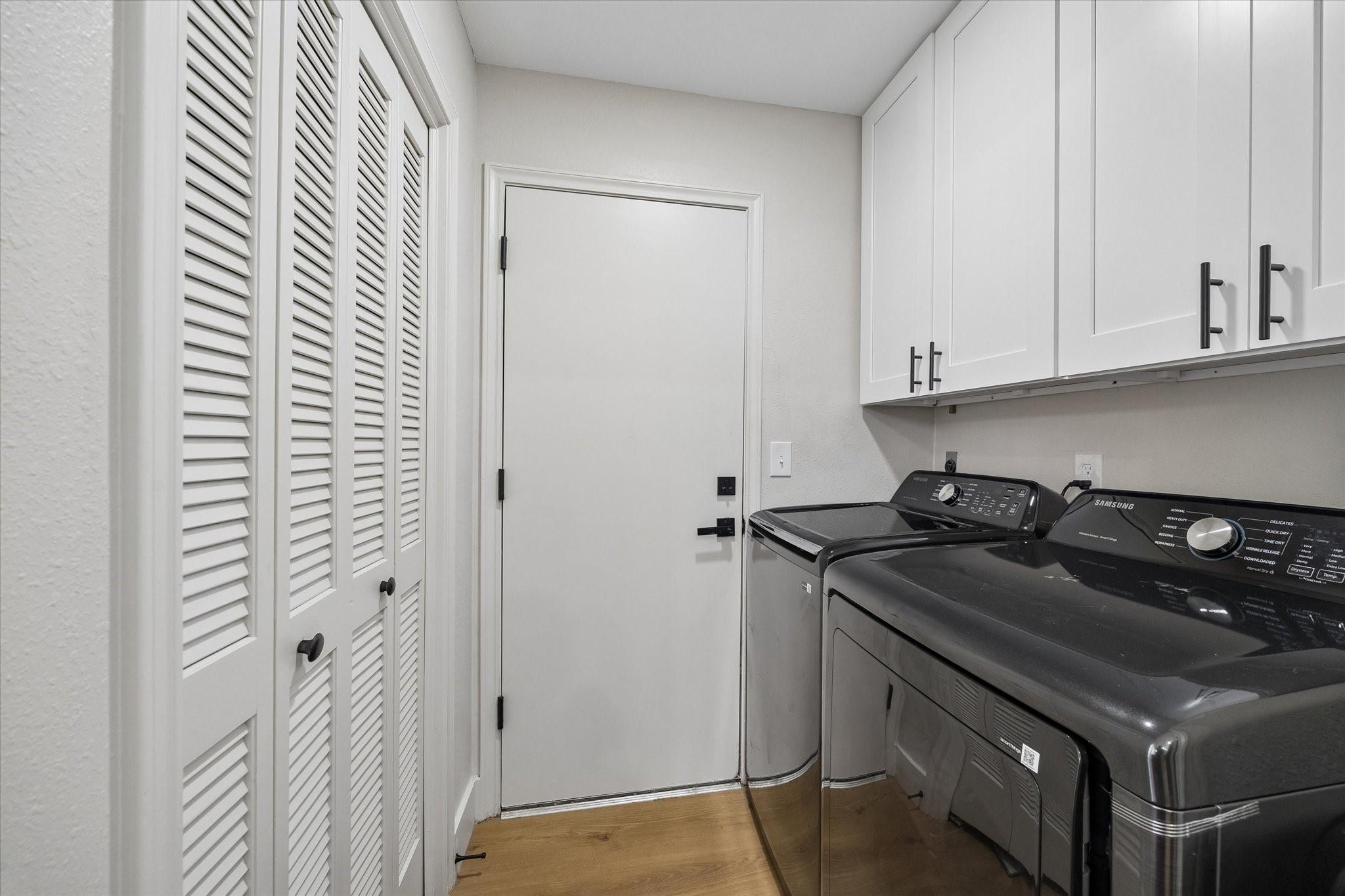 Sleek laundry room featuring ample white cabinetry, convenient closet storage and direct access to the two car garage.