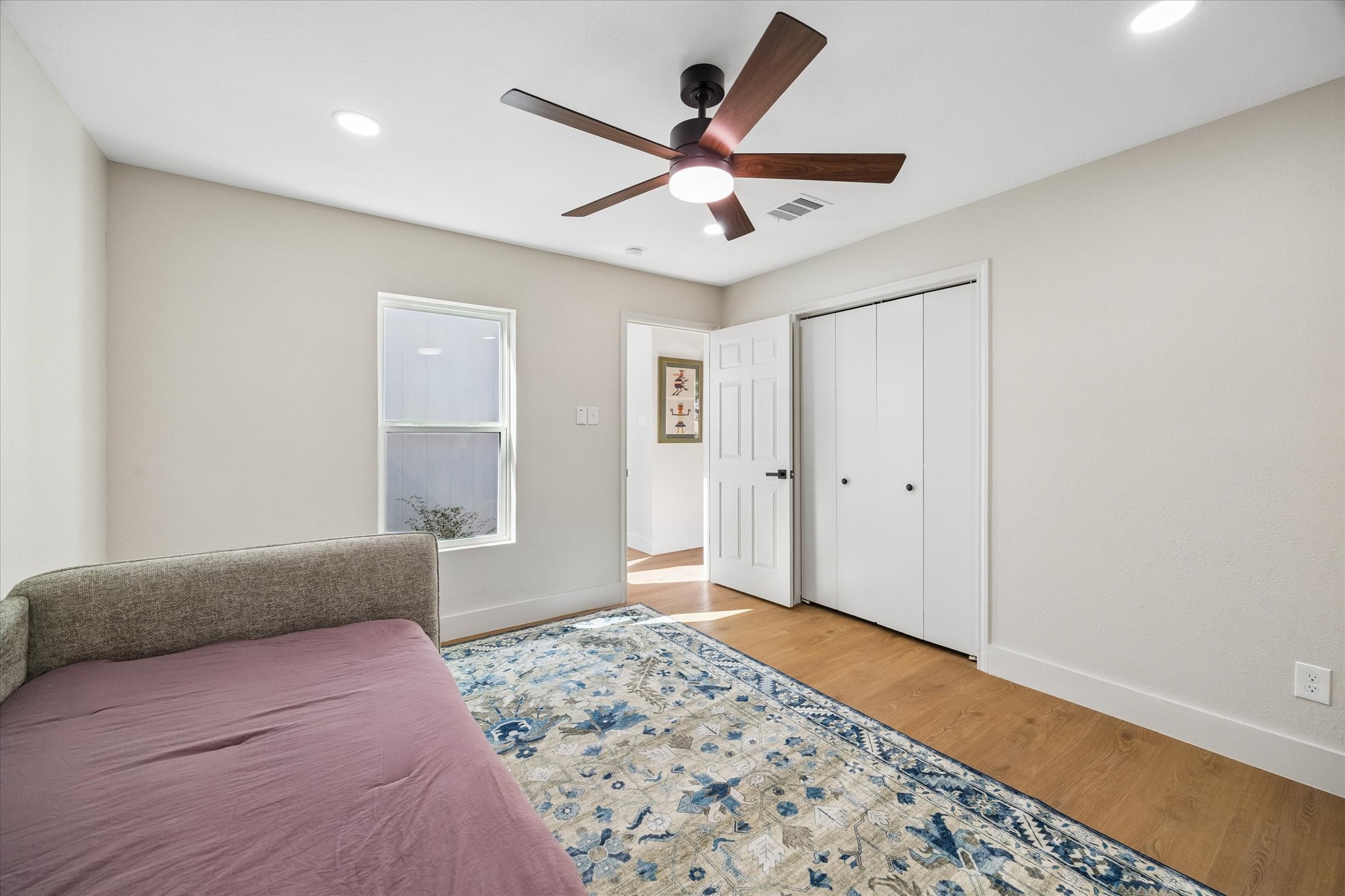 Bright, cozy bedroom featuring a stylish ceiling fan, warm hardwood floors, and ample closet space.