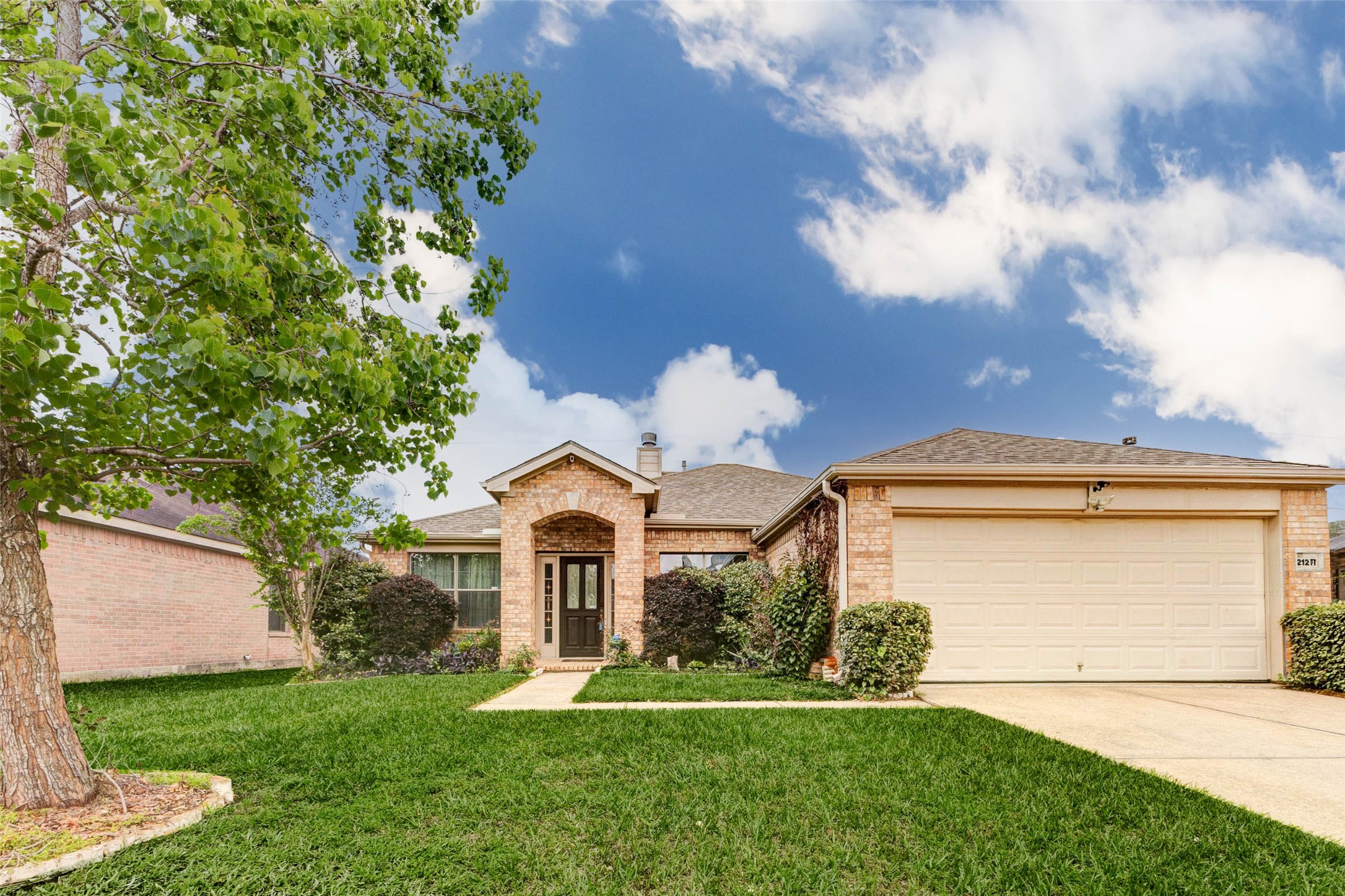 Picture-perfect front elevation featuring a classic brick faade, spacious two-car garage, and manicured lawn. The inviting covered entryway adds architectural charm, while the wide driveway provides ample parking. Mature trees and well-maintained landscaping enhance the homes curb appeal, creating a welcoming environment that sets the tone for the comfort and functionality found inside.