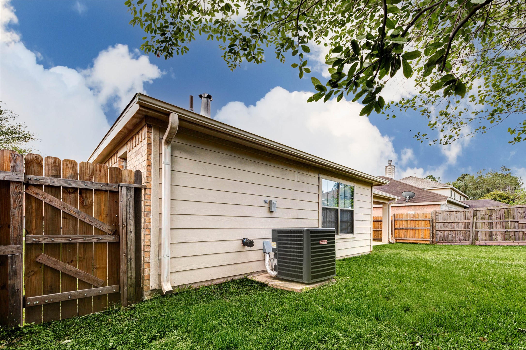 Side yard view showcasing the homes exterior construction and HVAC system placement for easy maintenance access. The fenced perimeter enhances privacy and security, while the open grassy area provides additional outdoor space. A practical layout that supports both functionality and low-maintenance living.