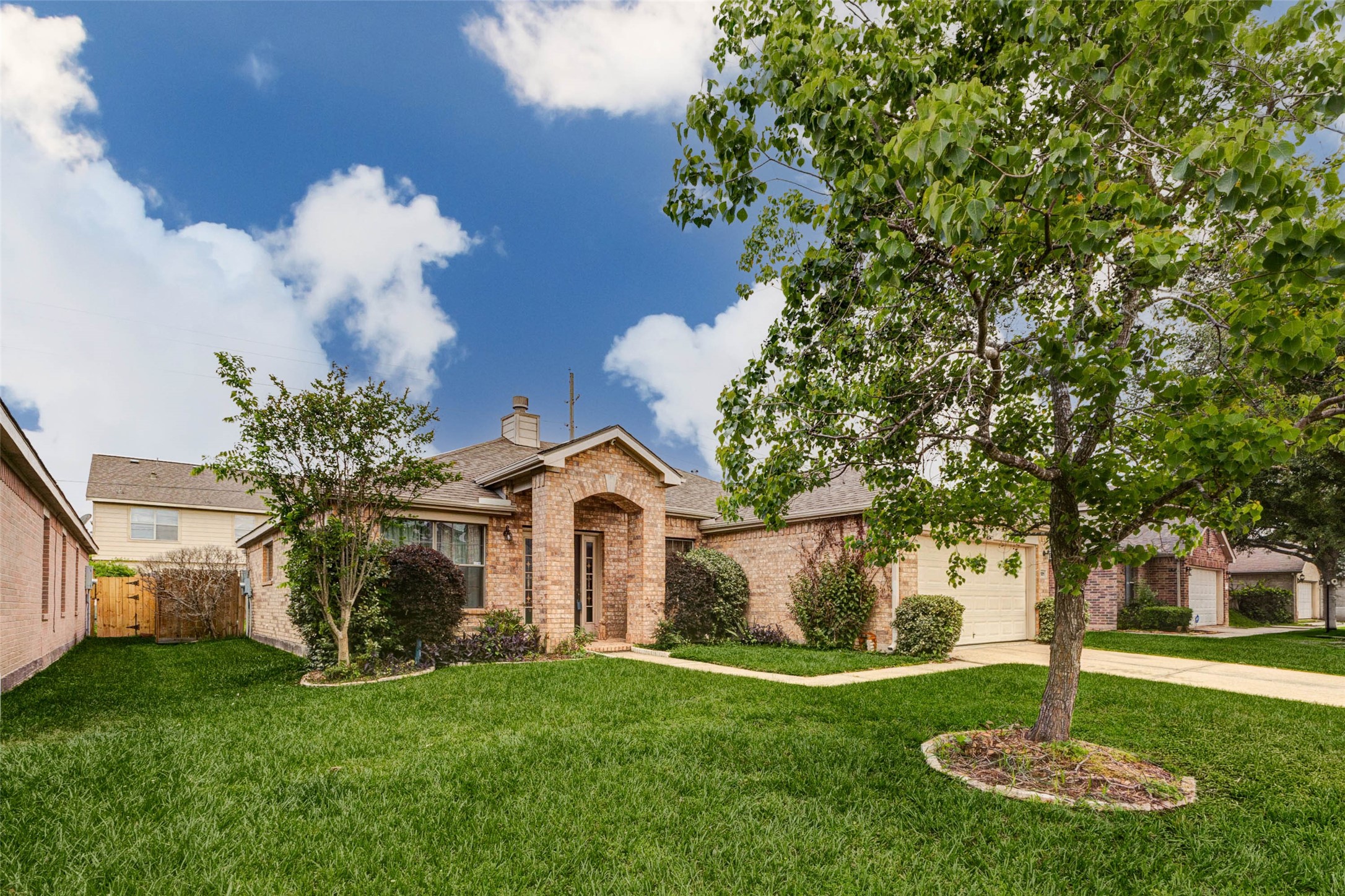 Welcoming curb appeal shines in this charming single-story brick home, framed by a lush green lawn and mature shade tree. A gently curved walkway leads to a covered arched entry, creating a warm and inviting first impression. Thoughtfully landscaped with trimmed shrubs and clean edges, the exterior reflects pride of ownership while offering a peaceful suburban setting perfect for everyday living.