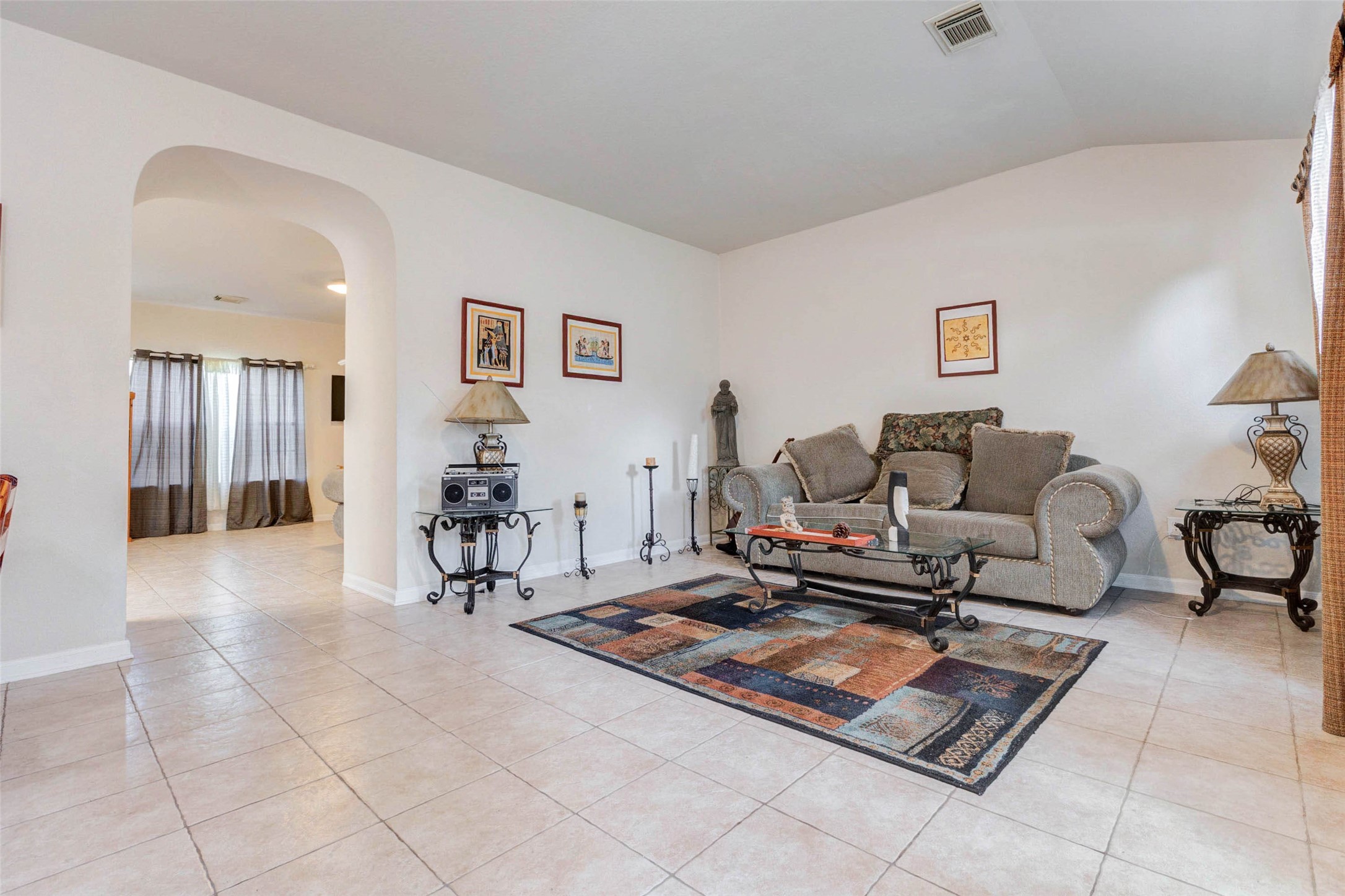 Comfortable living area featuring a cozy seating arrangement centered around a decorative rug and accent table. Natural light filters in from nearby windows, enhancing the warm and inviting atmosphere. The open layout connects effortlessly to other parts of the home, while neutral walls and tile flooring create a versatile space ready for your personal style and everyday relaxation.