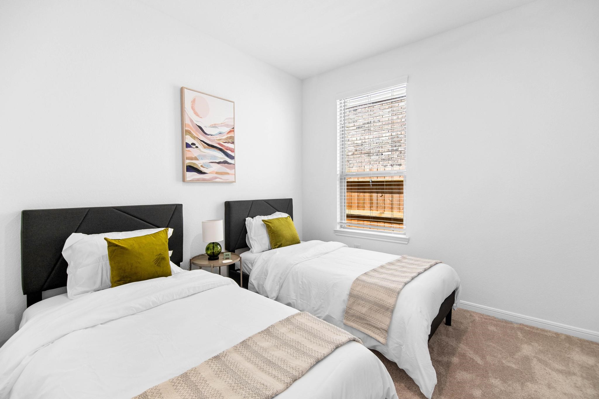 Bright and inviting bedroom with twin beds, plush pillows, and a tasteful piece of art, offering a cozy and comfortable space.