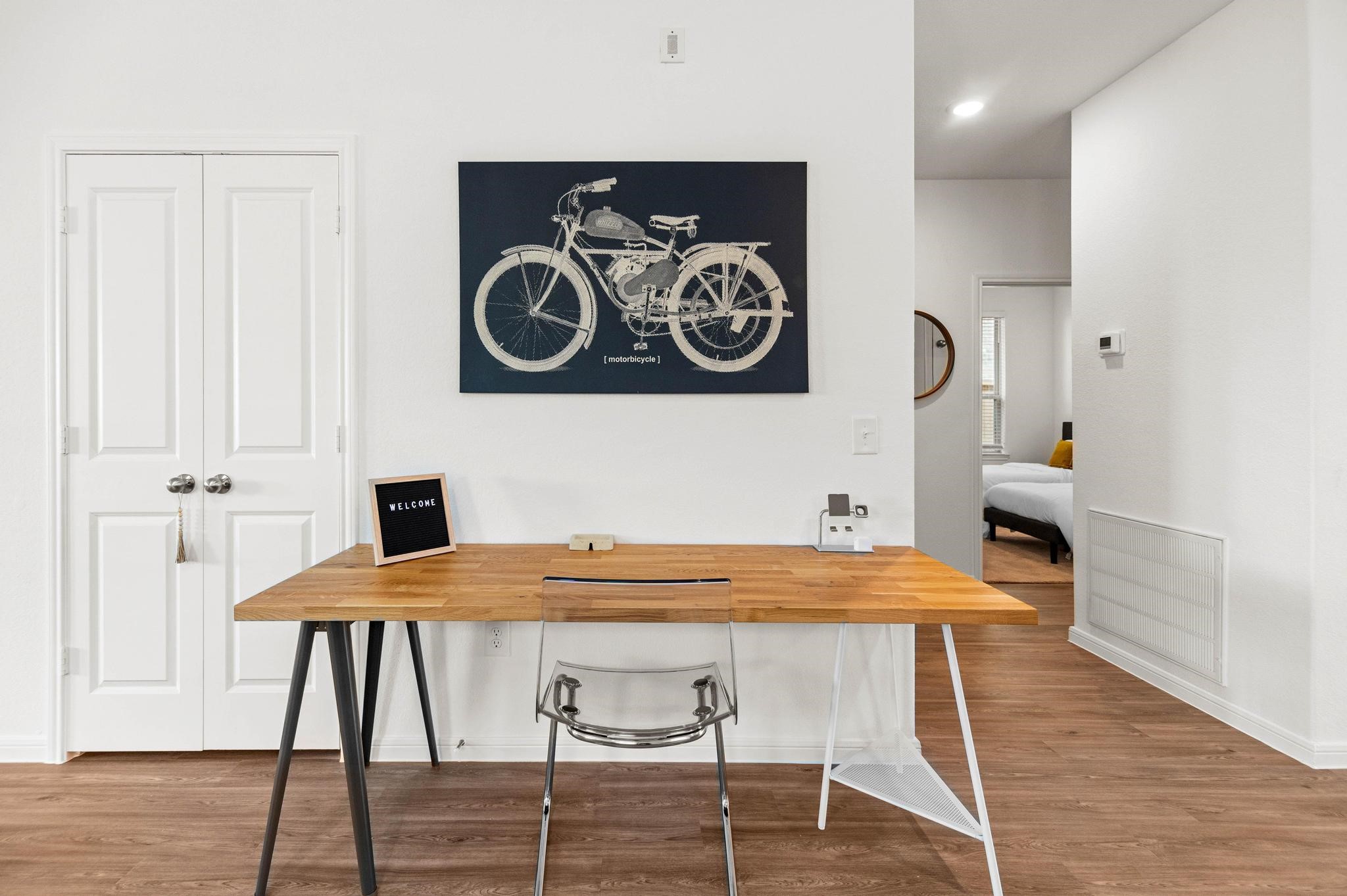Chic and modern workspace featuring a stylish wooden desk with a clear chair, set against a bright wall adorned with a vintage bicycle print. Chic and modern workspace featuring a stylish wooden desk with a clear chair, set against a bright wall adorned with a vintage bicycle print.