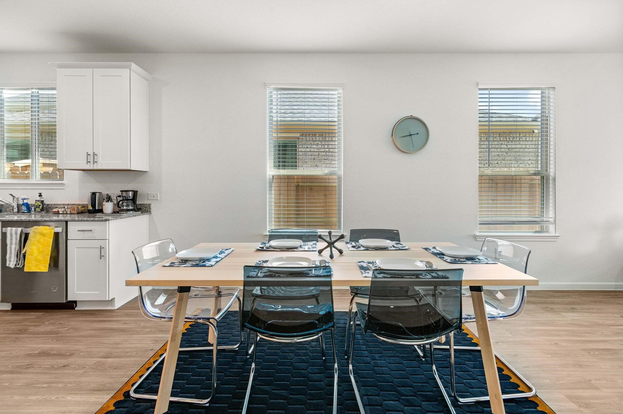 Bright and inviting dining area with a modern table setting, adjacent to a sleek kitchen featuring white cabinetry and stainless steel appliances.