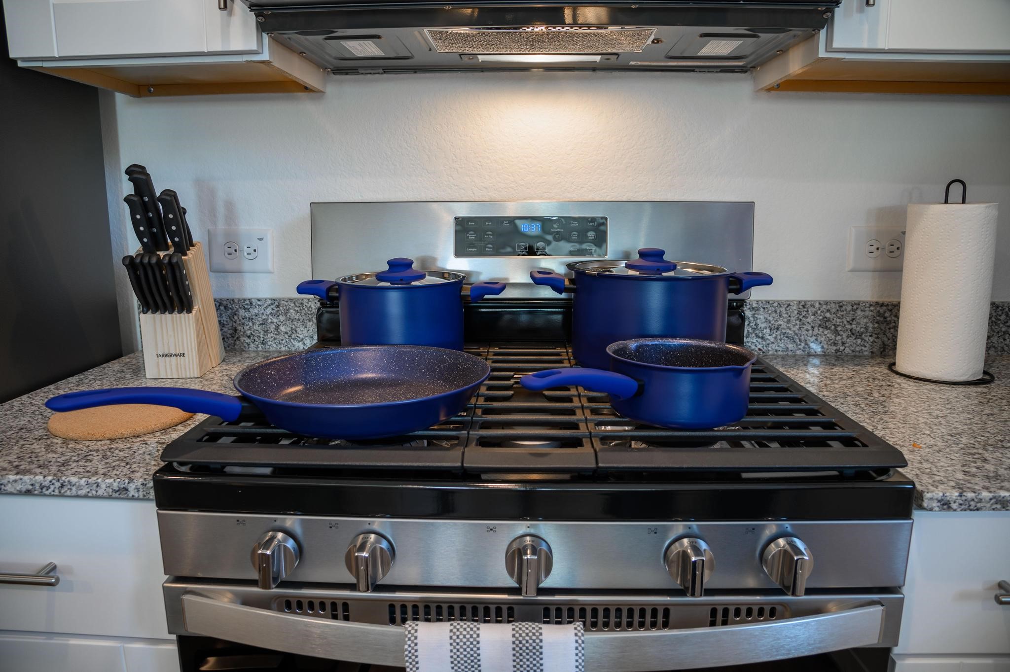 Modern kitchen with a sleek stainless steel gas stove, complemented by blue cookware and granite countertops, offering a stylish and functional cooking space.