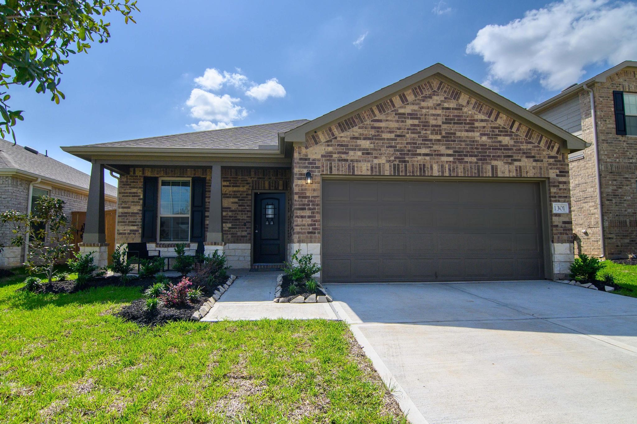 Charming single-story brick home with an inviting front porch, well-maintained landscaping, and a spacious two-car garage.