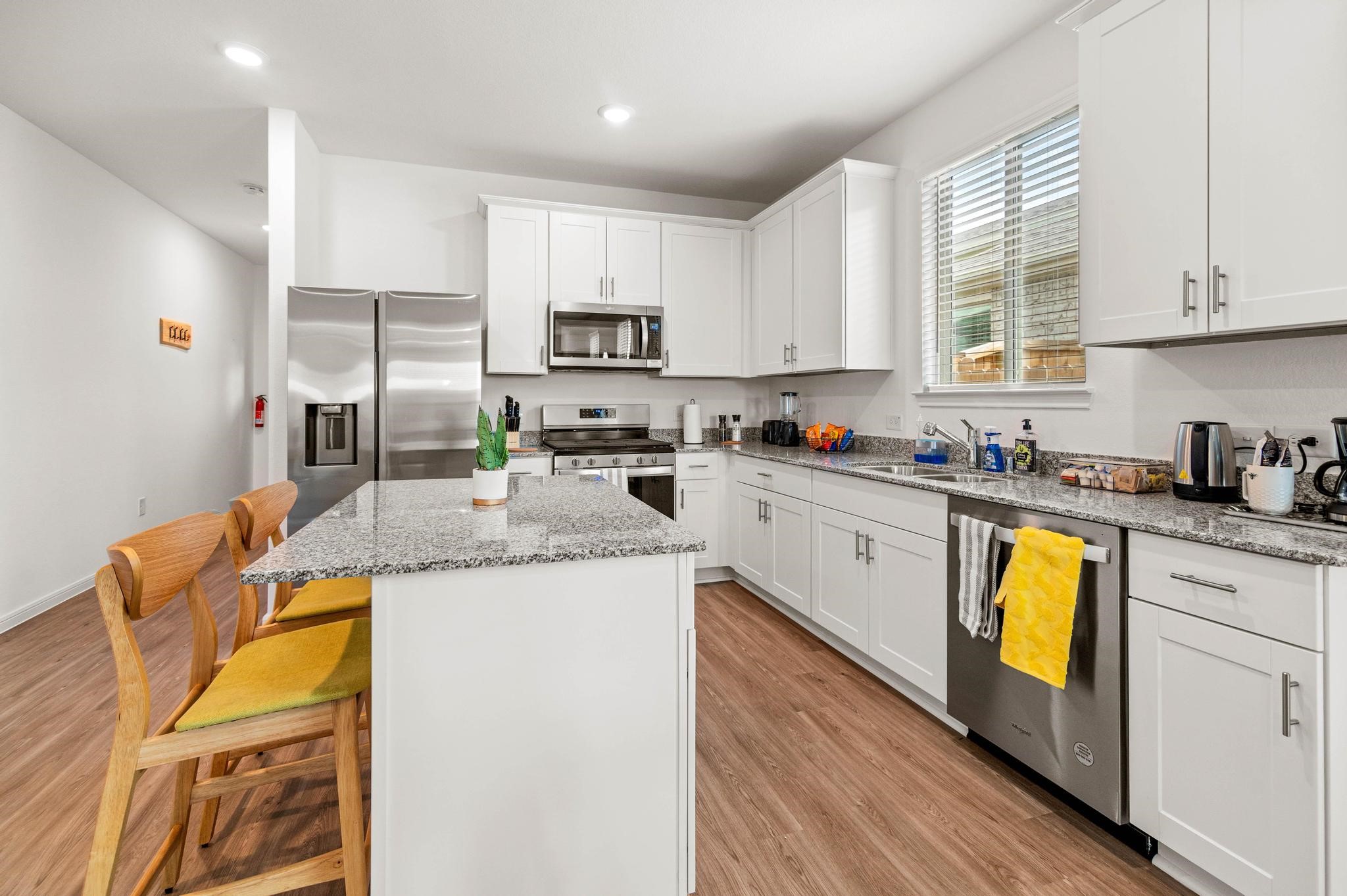 Modern kitchen with sleek stainless steel appliances, granite countertops, and ample white cabinetry, complemented by a cozy breakfast bar and warm wood flooring.
