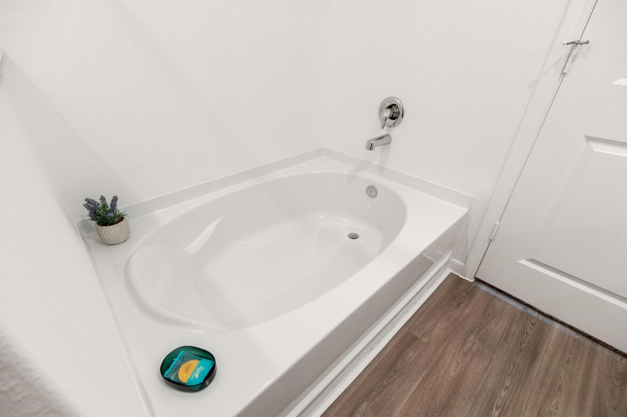 Modern bathroom featuring a sleek soaking tub with chrome fixtures, complemented by elegant wood-style flooring for a spa-like experience.