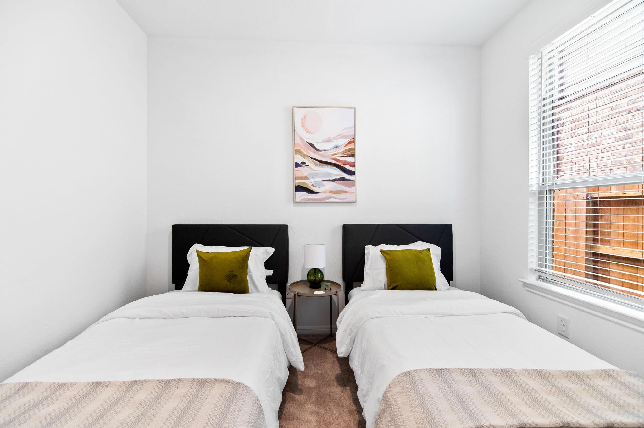 Cozy bedroom featuring two twin beds with plush pillows, a stylish nightstand, and abundant natural light from a large window.