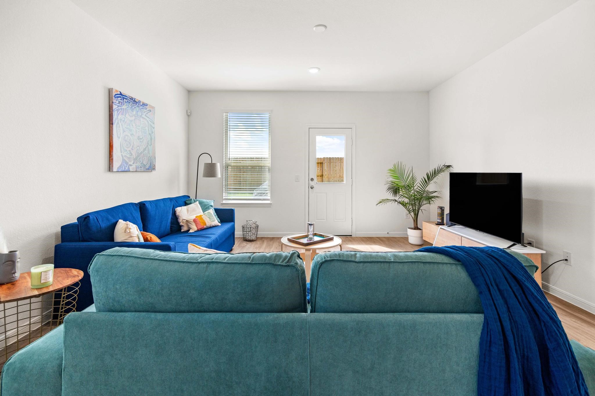 Bright and inviting living room featuring cozy blue sofas, a stylish coffee table, and a modern entertainment setup, all enhanced by natural light and a touch of greenery.
