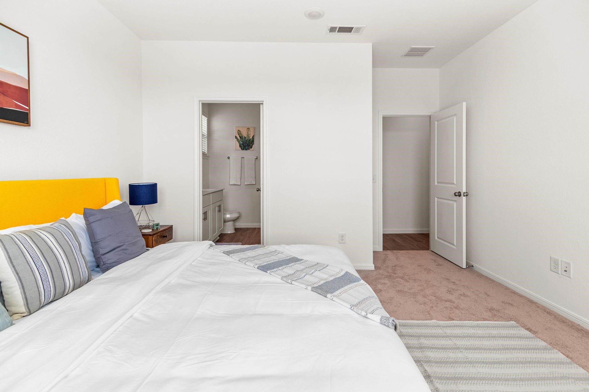 Bright and inviting bedroom featuring a cozy bed with a vibrant yellow headboard, plush carpeting, and convenient access to an en-suite bathroom.
