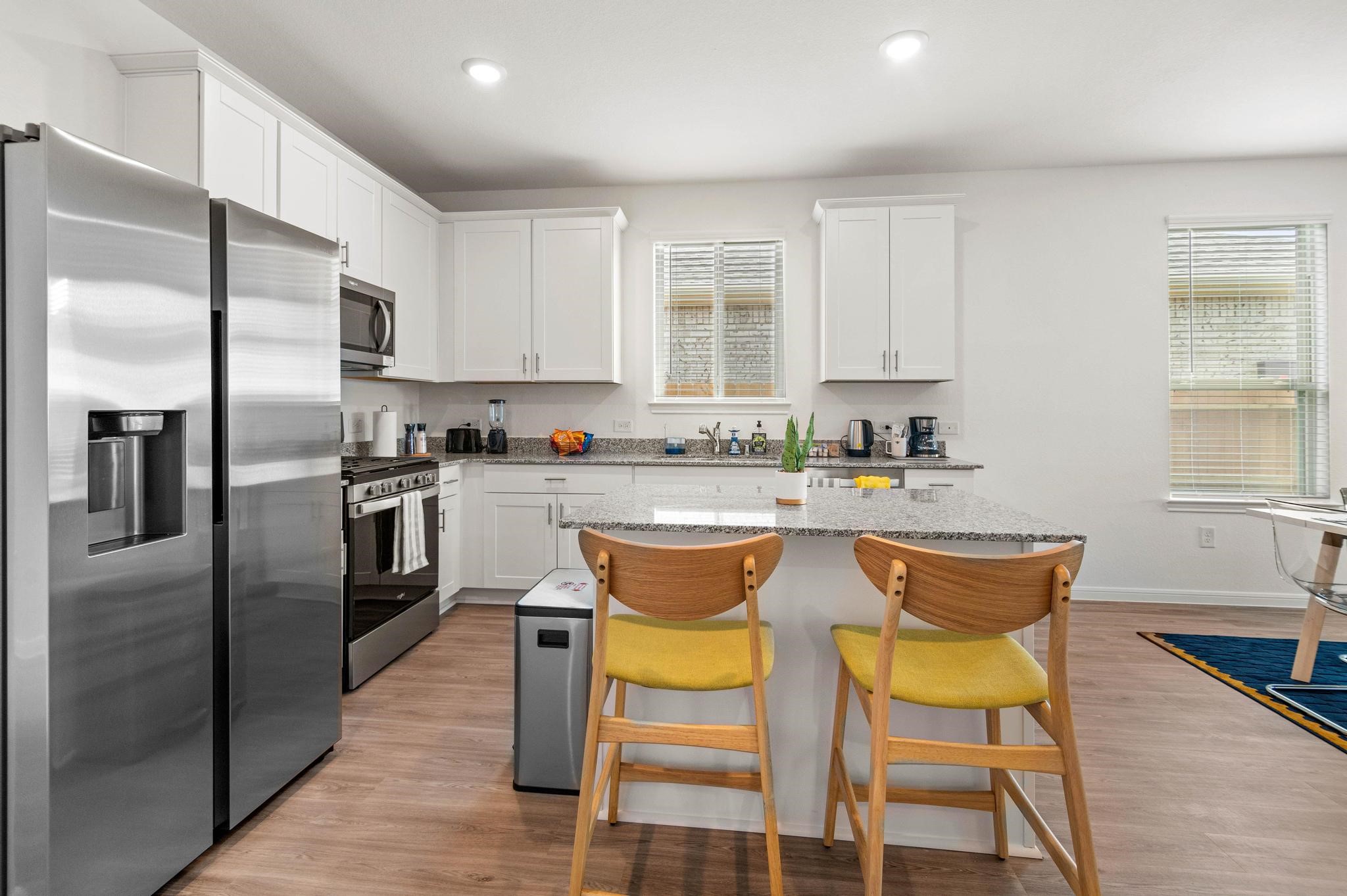 Modern kitchen with sleek stainless steel appliances, white cabinetry, and a spacious granite island featuring stylish bar seating.