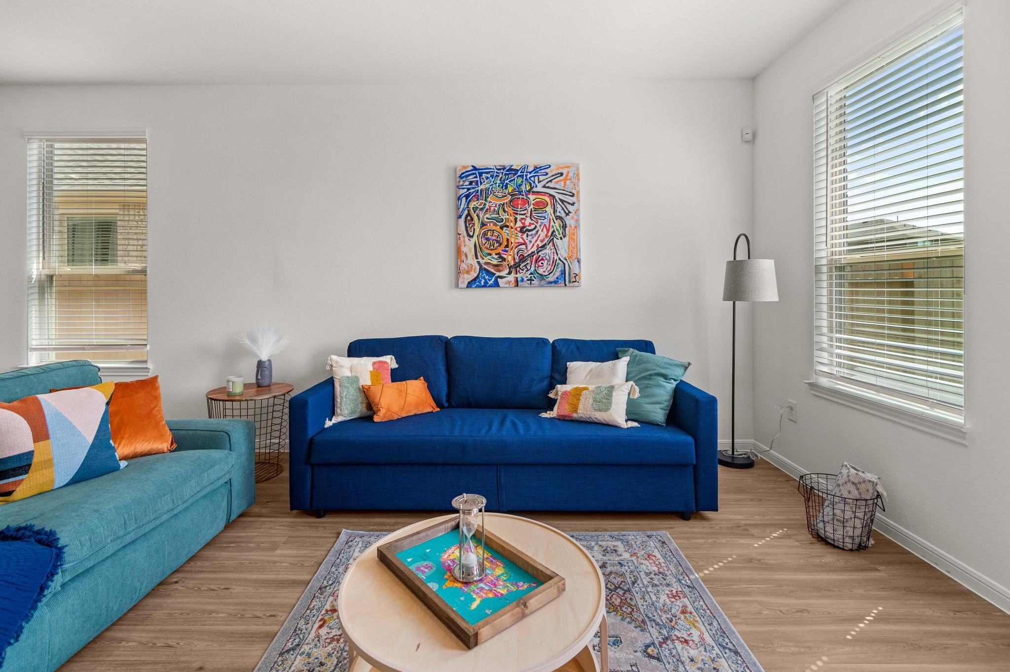 Bright and inviting living room with vibrant blue sofas, colorful cushions, and modern artwork, complemented by large windows that fill the space with natural light.