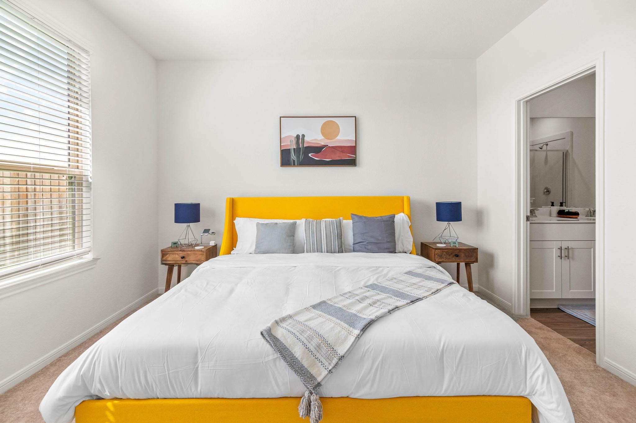 Bright and inviting bedroom featuring a bold yellow bed frame, stylish side tables with modern lamps, and direct access to an en-suite bathroom.