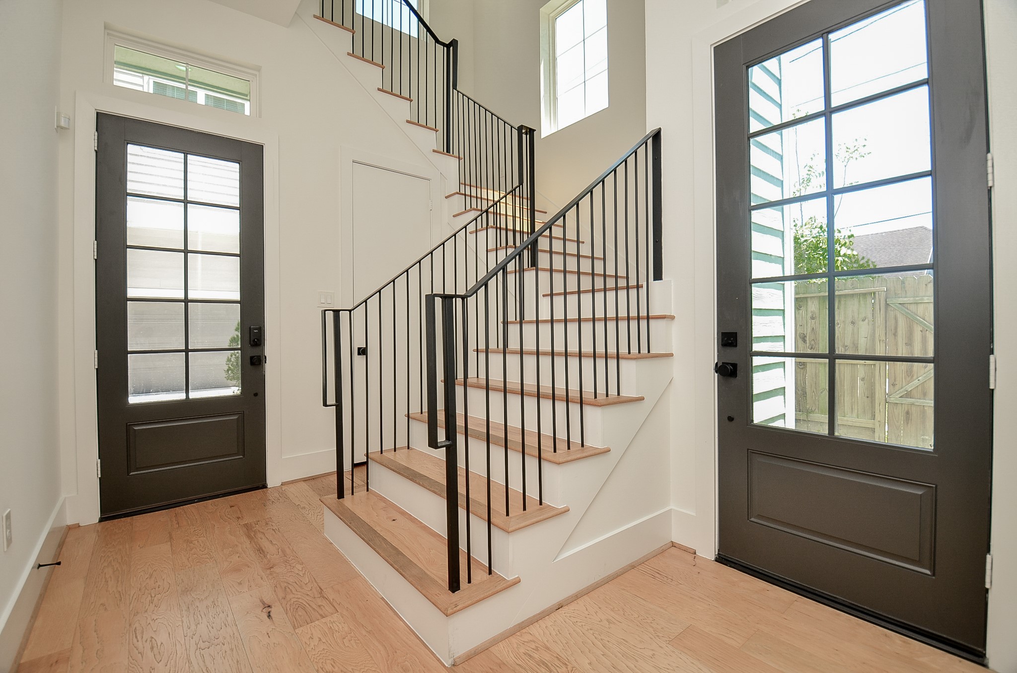 Ground-floor entry with wood flooring, coat closet, access to backyard, and a beautiful staircase with iron spindles leading to the main living area.