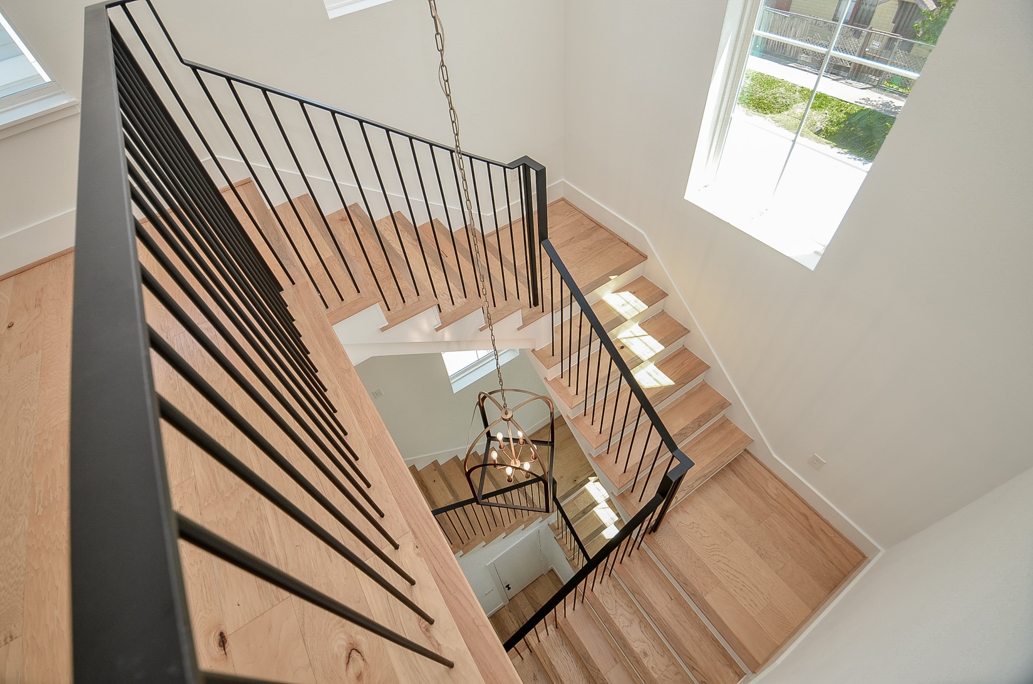 From the top of the staircase, enjoy a striking view spanning all three levels, highlighted by the rich wood steps and sleek black railings that add a bold, modern touch to the homes design.
