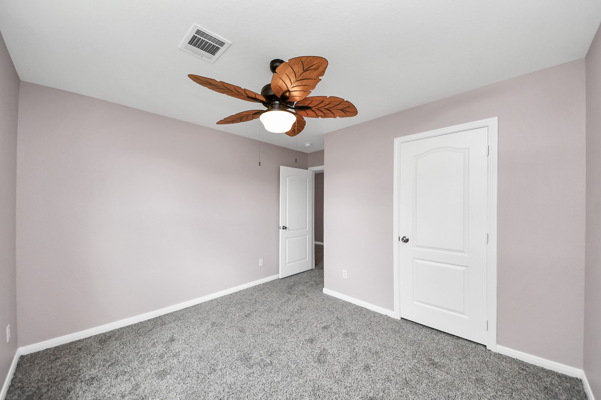 Discover the charm of Bedroom #2, featuring soft lavender walls, plush carpeting, and a unique leaf-shaped ceiling fan that adds a touch of elegance and comfort.