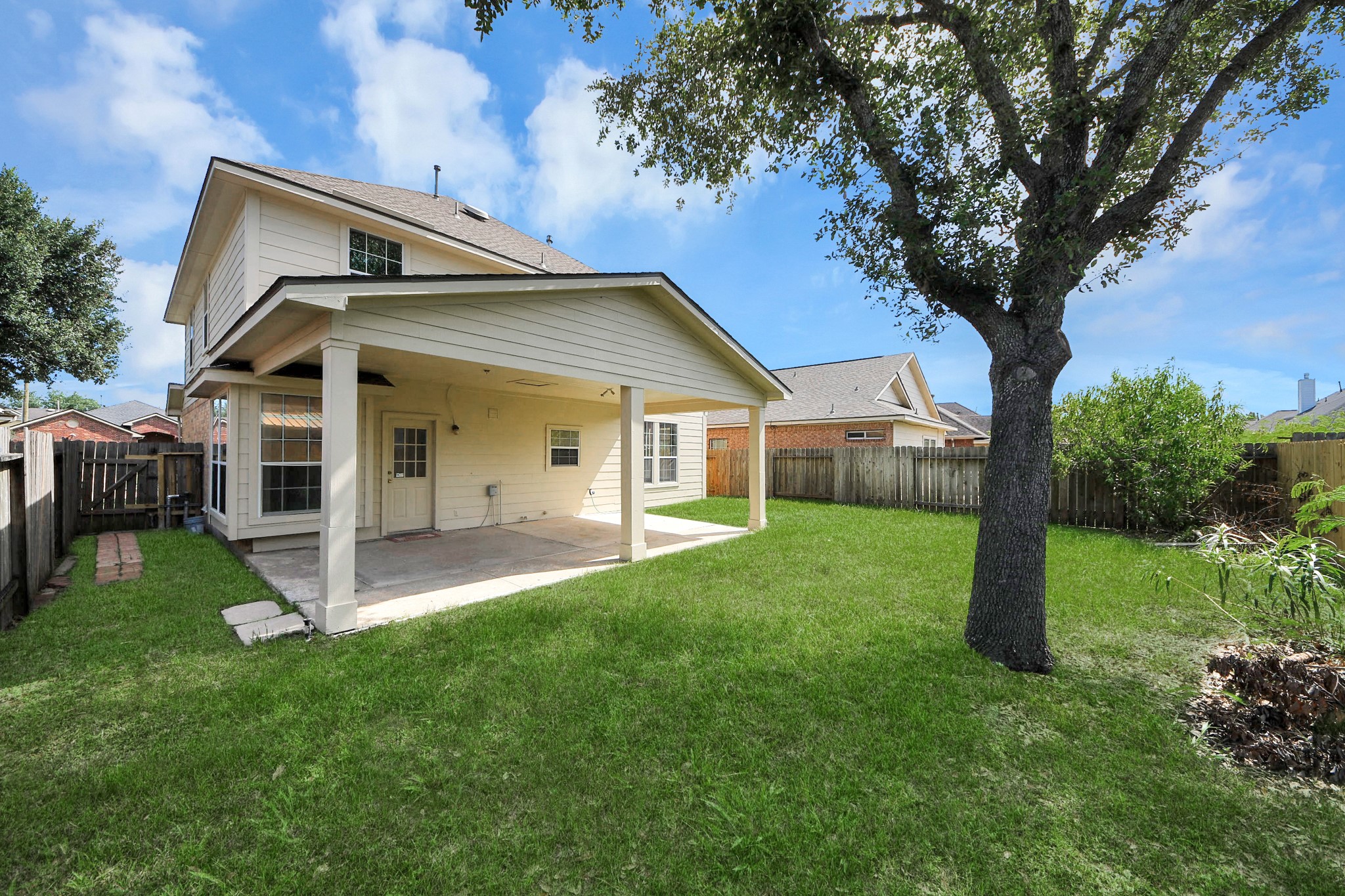 Charming two-story home with a spacious covered patio, perfect for outdoor gatherings, set in a lush, fenced backyard shaded by mature trees.