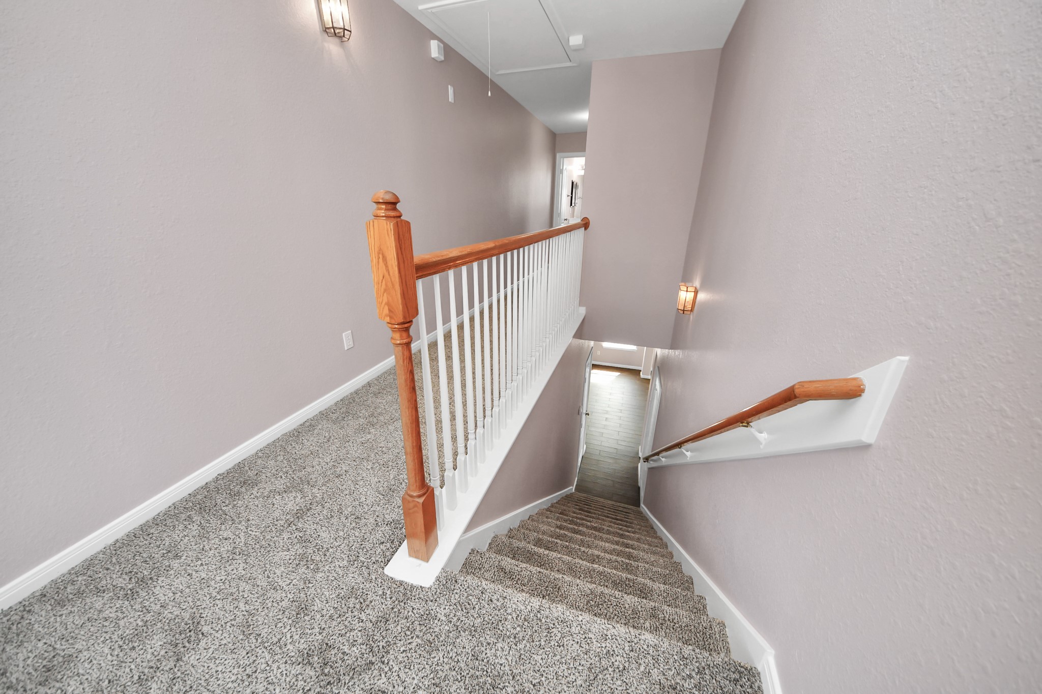 Carpeted stairs with a wooden handrail lead to a bright landing, accented by soft wall sconces and neutral wall tones.