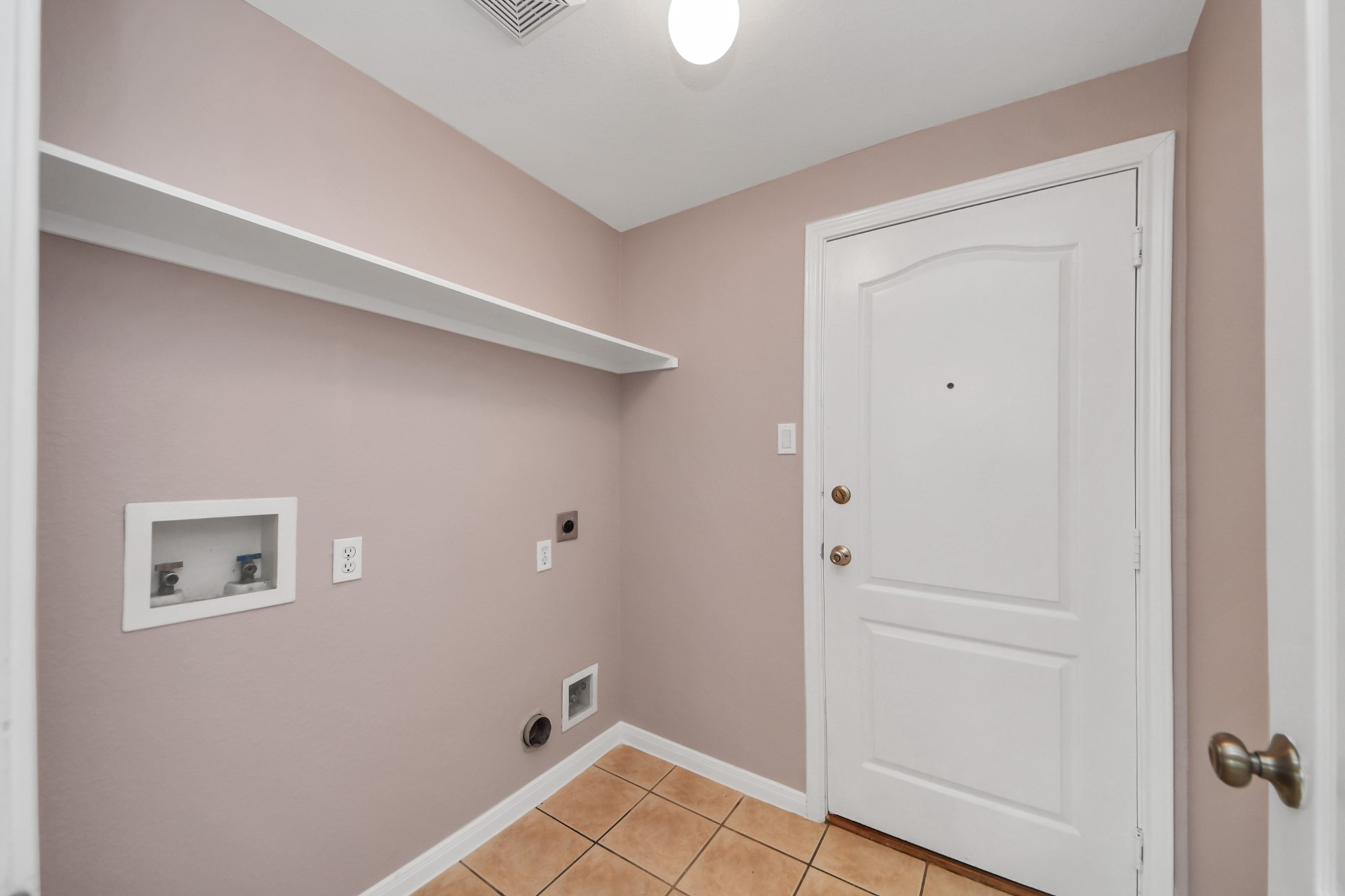 Spacious laundry room with hookups, tile flooring, and convenient shelving for storage.