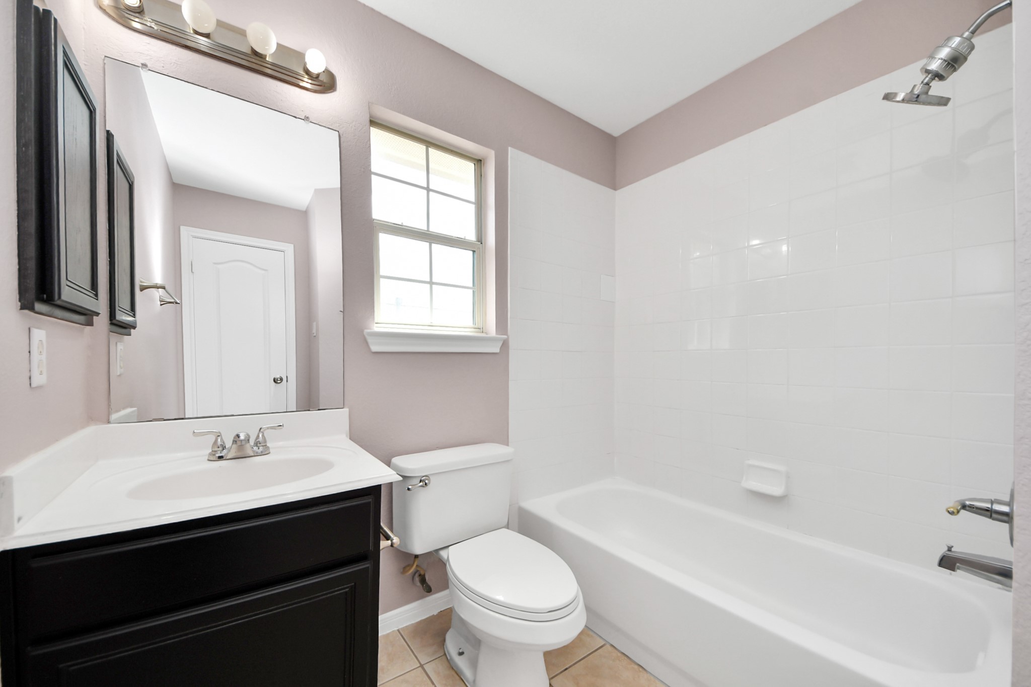Bright and inviting bathroom featuring a sleek vanity with ample storage, a classic bathtub with a shower, and a large window providing natural light.