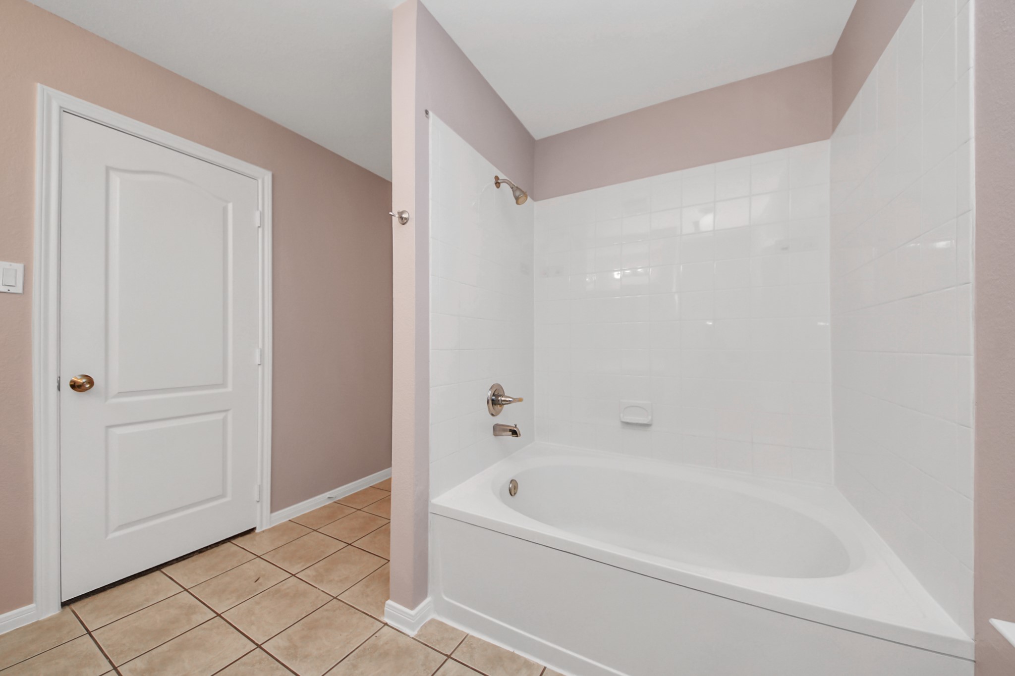 Spacious primary bathroom featuring a sleek white bathtub with tiled surround and a neutral color palette, offering a clean and modern feel.