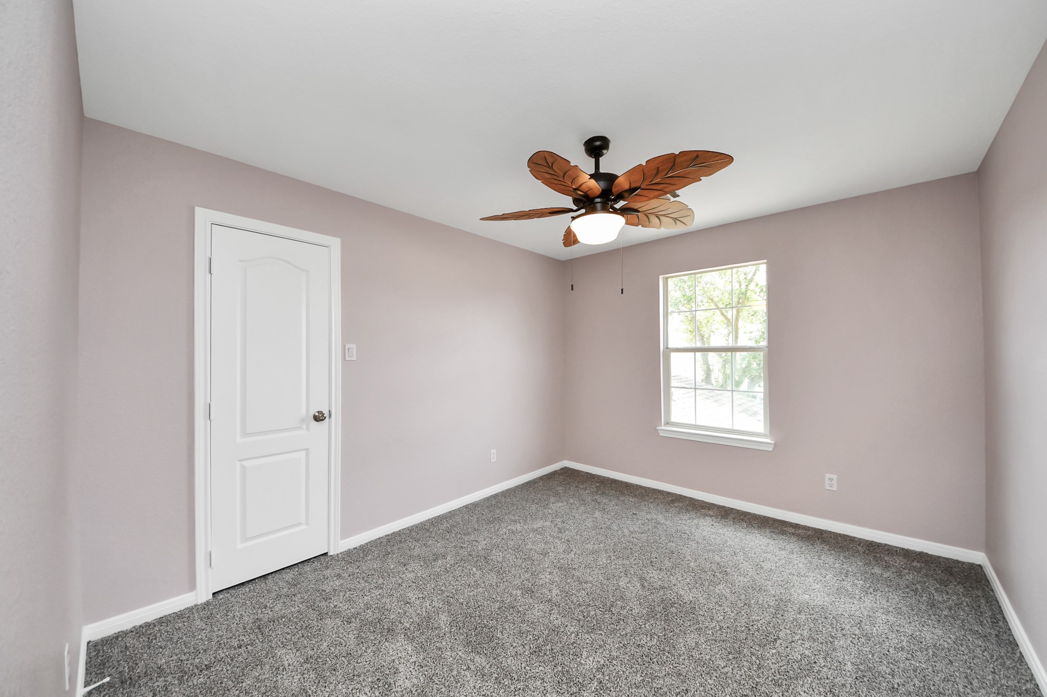 Experience comfort in this inviting bedroom featuring plush carpeting, a unique ceiling fan, and abundant natural light through a large window.