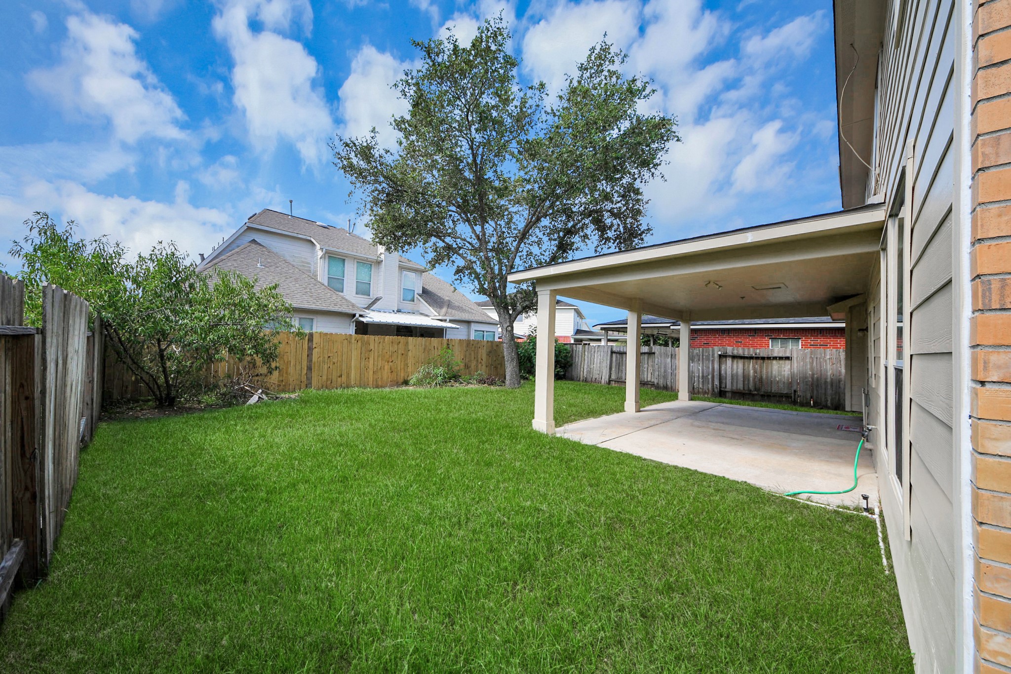Spacious backyard with lush green lawn, a covered patio perfect for outdoor gatherings, and privacy fencing for a serene atmosphere.