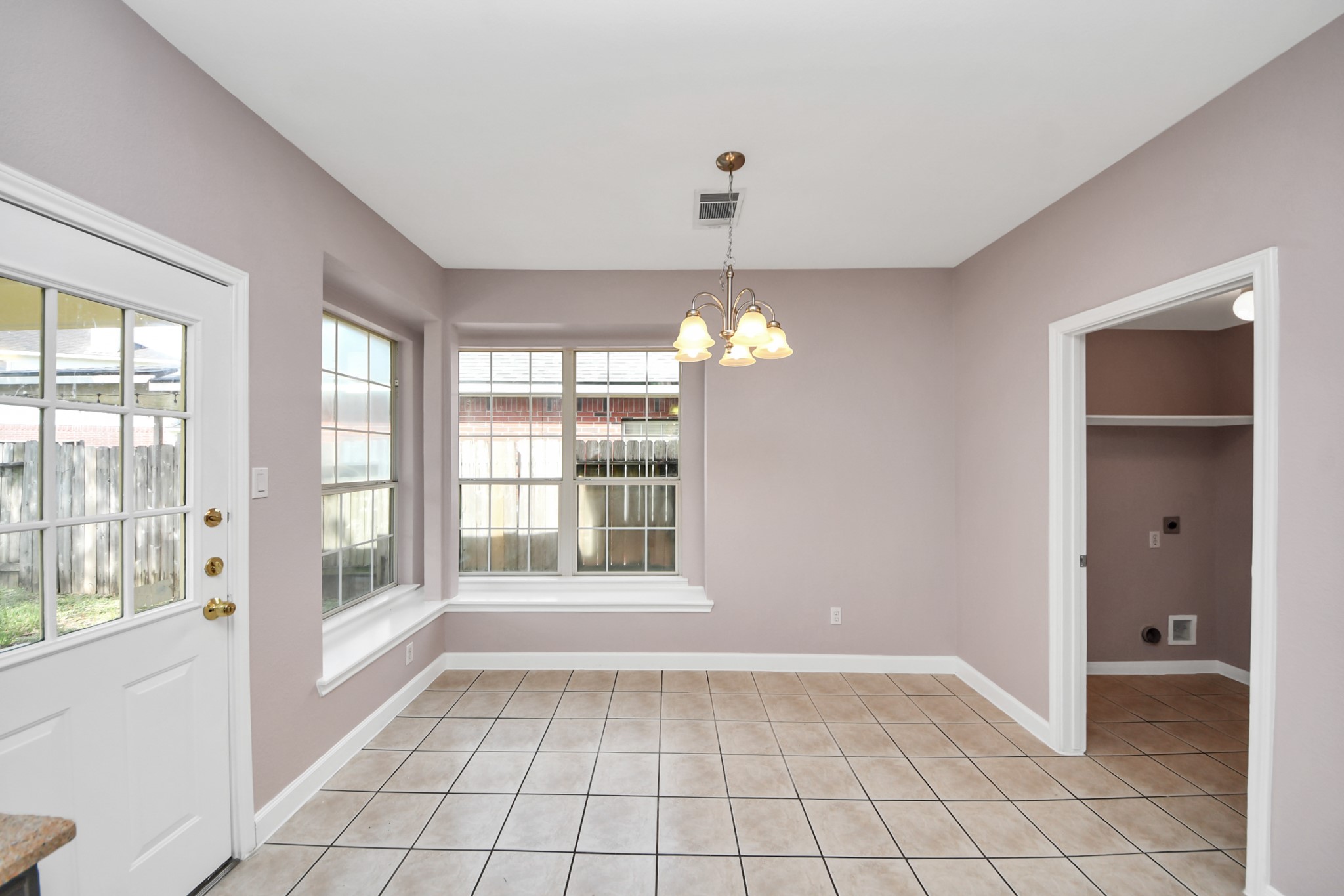 Bright and inviting dining area with large windows, tile flooring, and a stylish light fixture, offering easy access to the backyard through a side door.