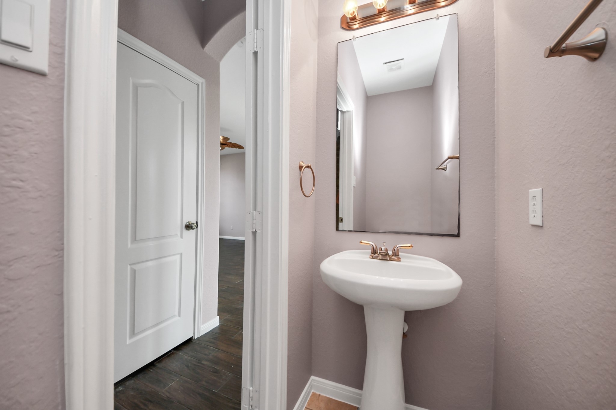 Charming half-bathroom features a pedestal sink, elegant mirror, and warm lighting, complemented by soft, neutral walls.