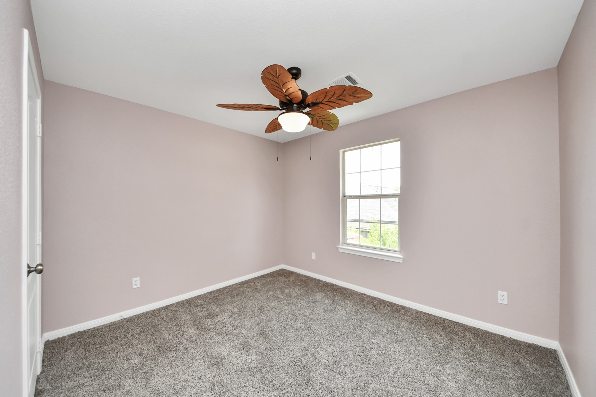 Bright and inviting, this spacious bedroom features plush carpeting, soft pastel walls, and a unique ceiling fan, offering a cozy retreat with ample natural light.
