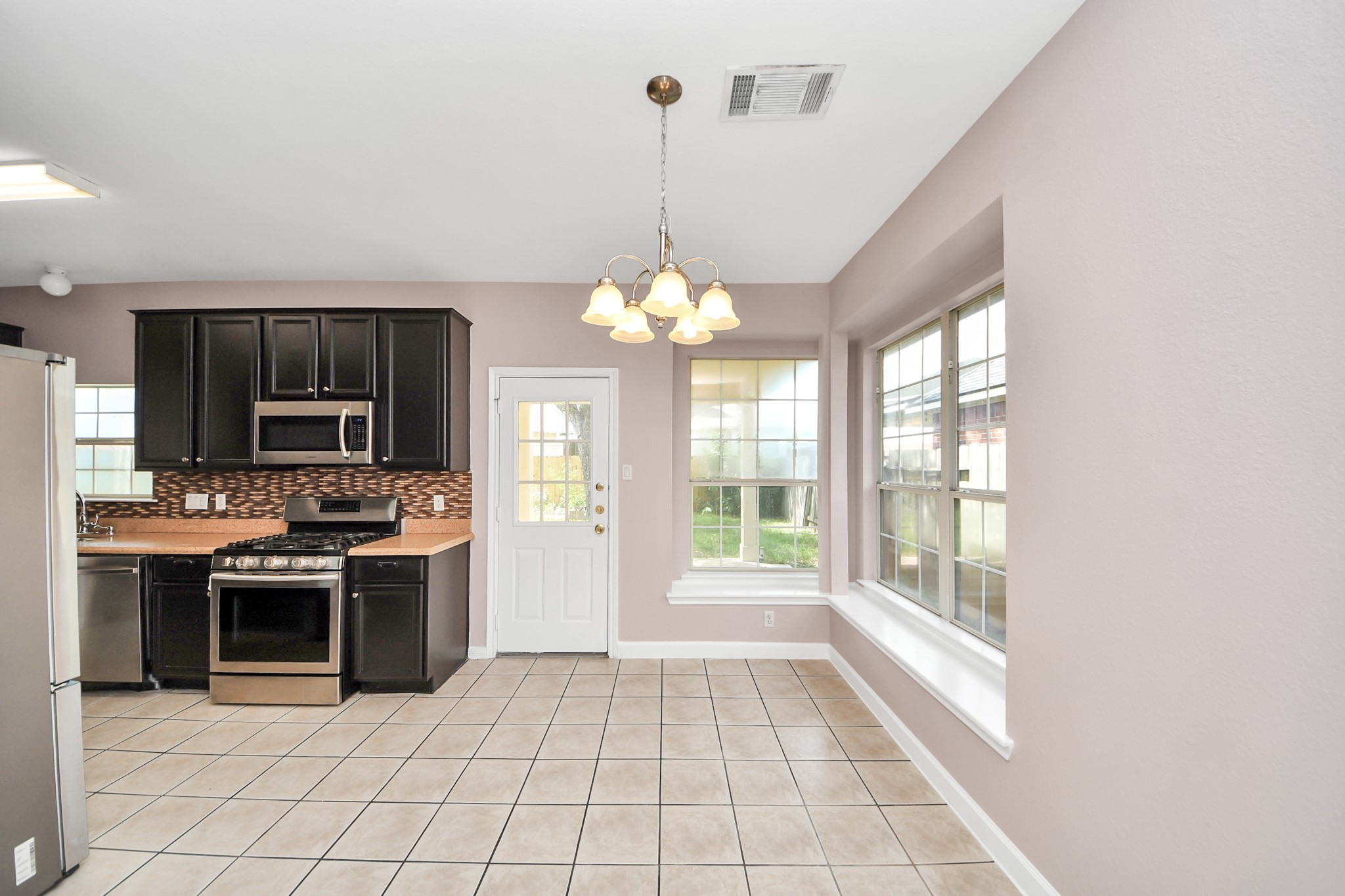 Bright kitchen and dining area with modern dark cabinetry, stainless steel appliances, and large windows offering abundant natural light.