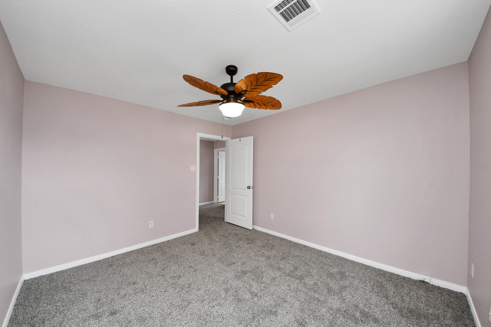 Experience tranquility in this spacious bedroom featuring soft lavender walls, plush carpet, and a stylish leaf-inspired ceiling fan.