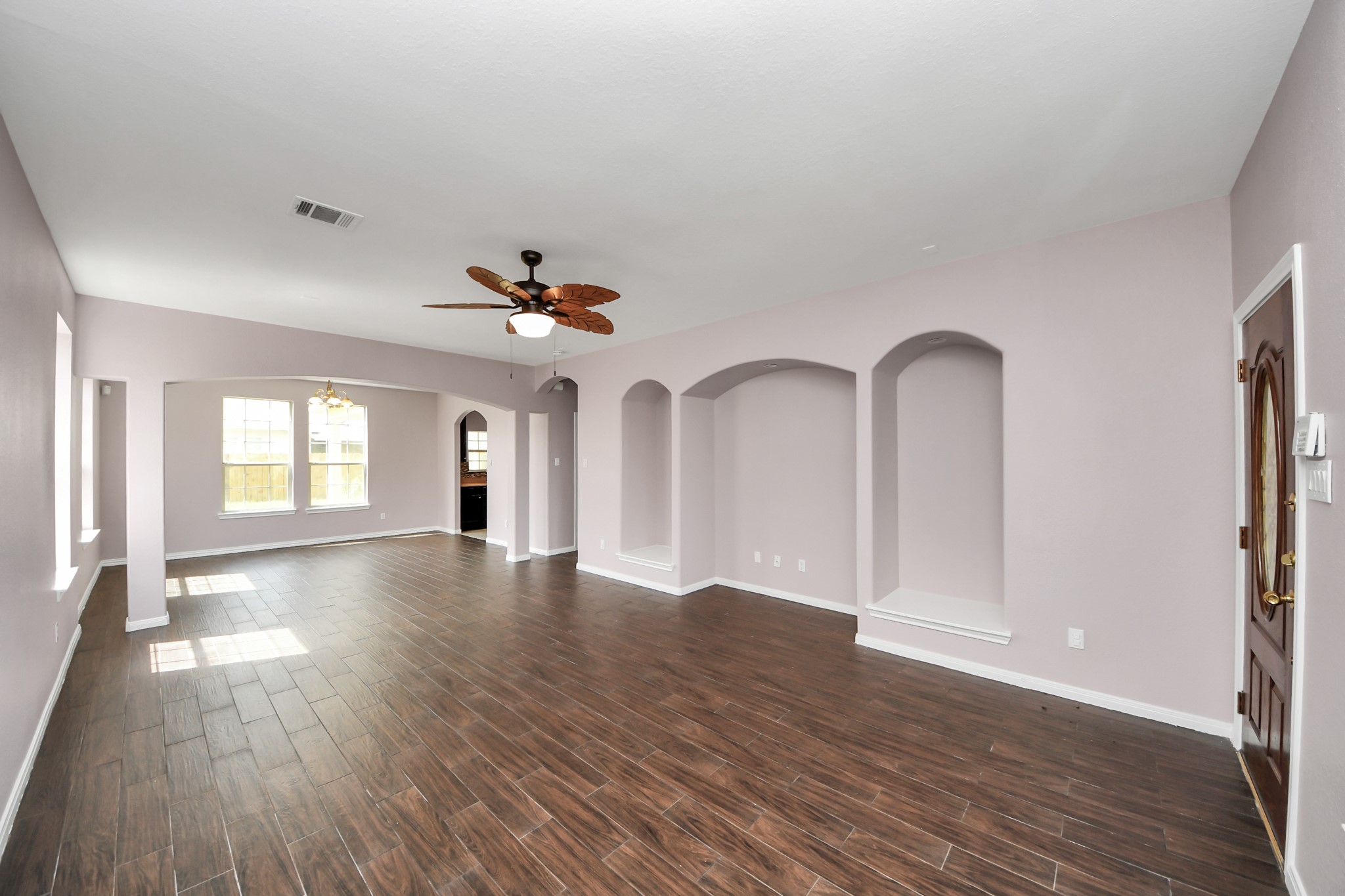 Spacious living area with rich wood-look flooring, built-in alcoves, and abundant natural light from large windows.
