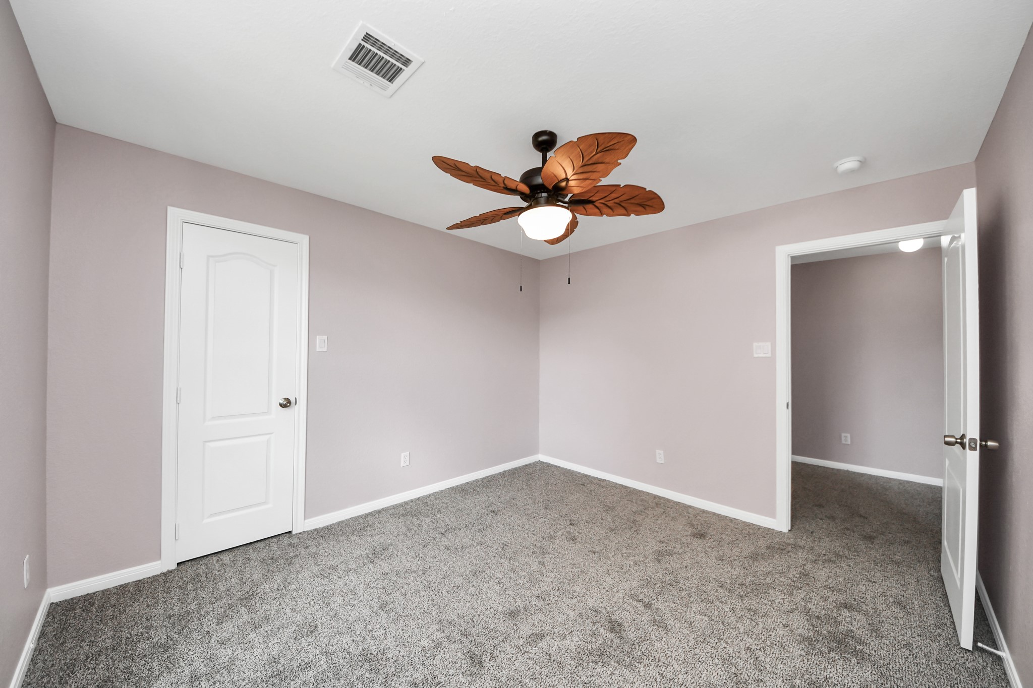 Discover tranquility in this cozy bedroom featuring soft lavender walls, plush carpeting, and a stylish ceiling fan for the perfect retreat.
