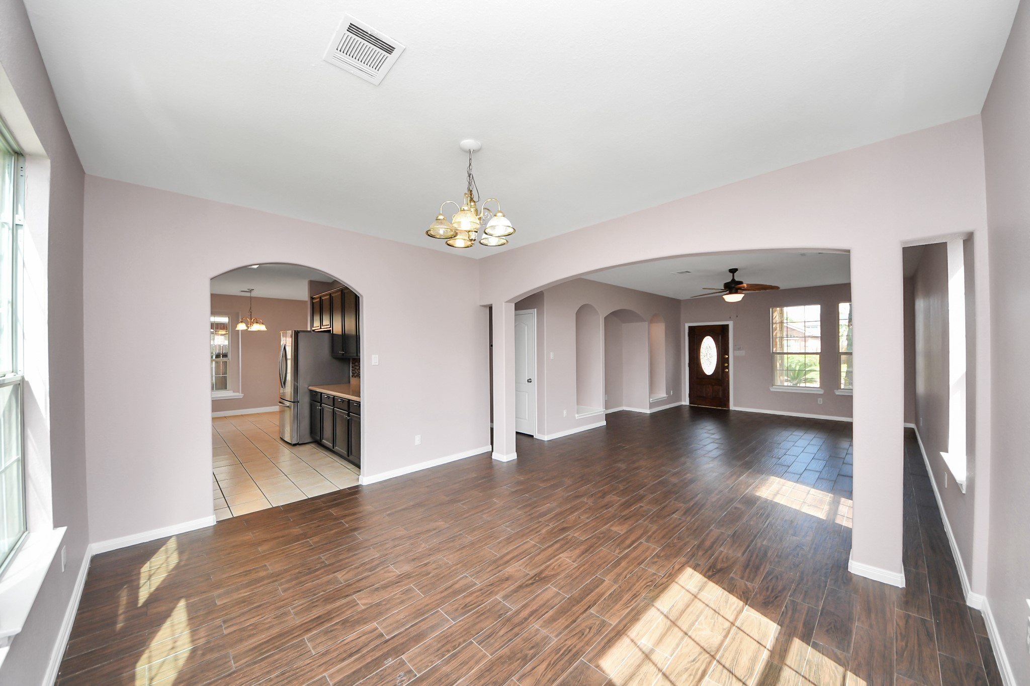 Spacious open-concept living area with elegant wood-look flooring, archways leading to a modern kitchen, and ample natural light from large windows.