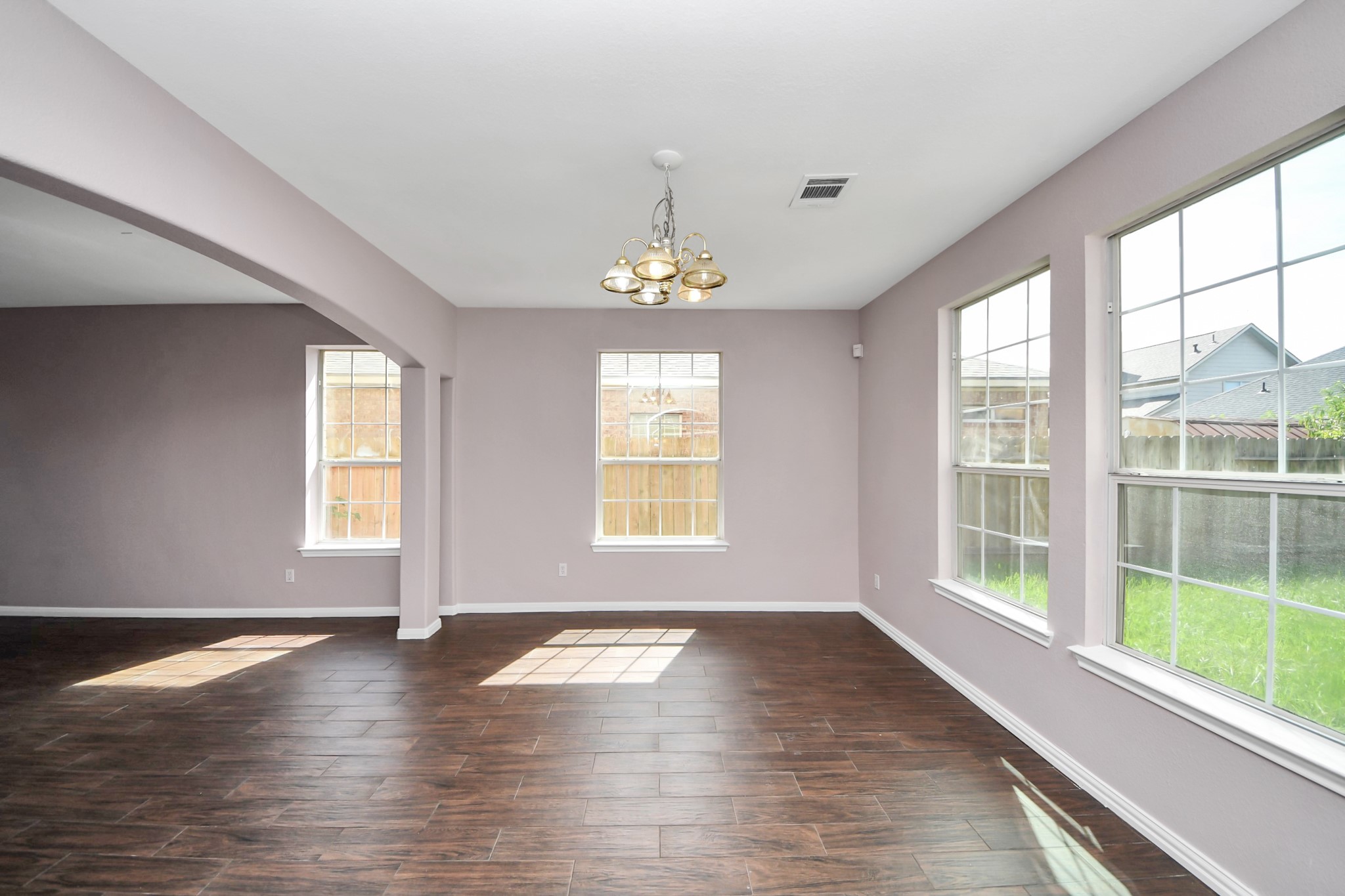 Bright and spacious living area with large windows, elegant wood-look flooring, and a stylish chandelier, perfect for entertaining and relaxation.