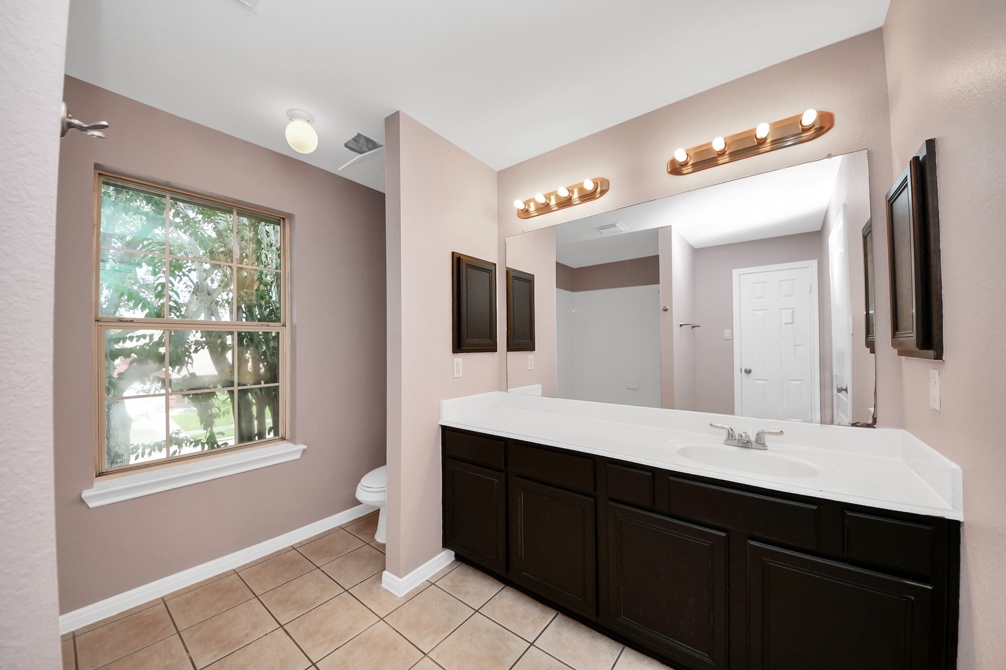 Spacious primary bathroom featuring a large vanity with dual sinks, elegant lighting, and a window that brings in natural light, complemented by a soothing color palette.