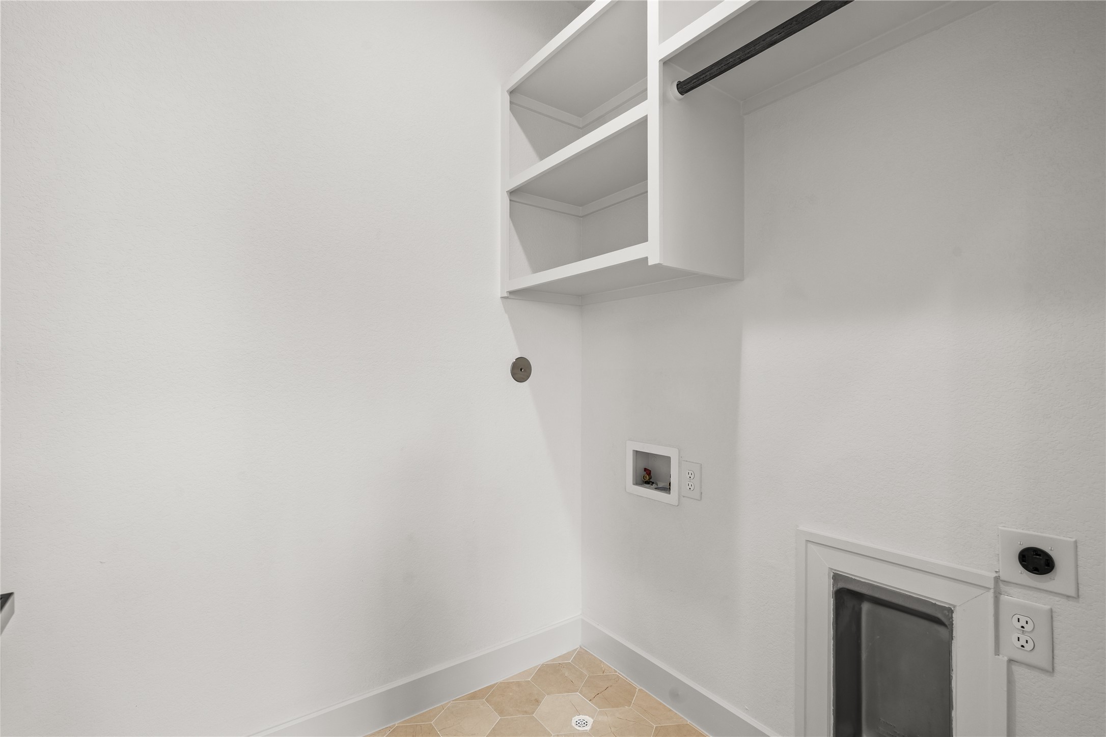The dedicated laundry room features custom white cabinets, built-in shelving, and a hanging drying rod. The utility wall includes washer and dryer hookups with heavy-duty outlets, all set against an easy-to-clean, geometric tile floor.