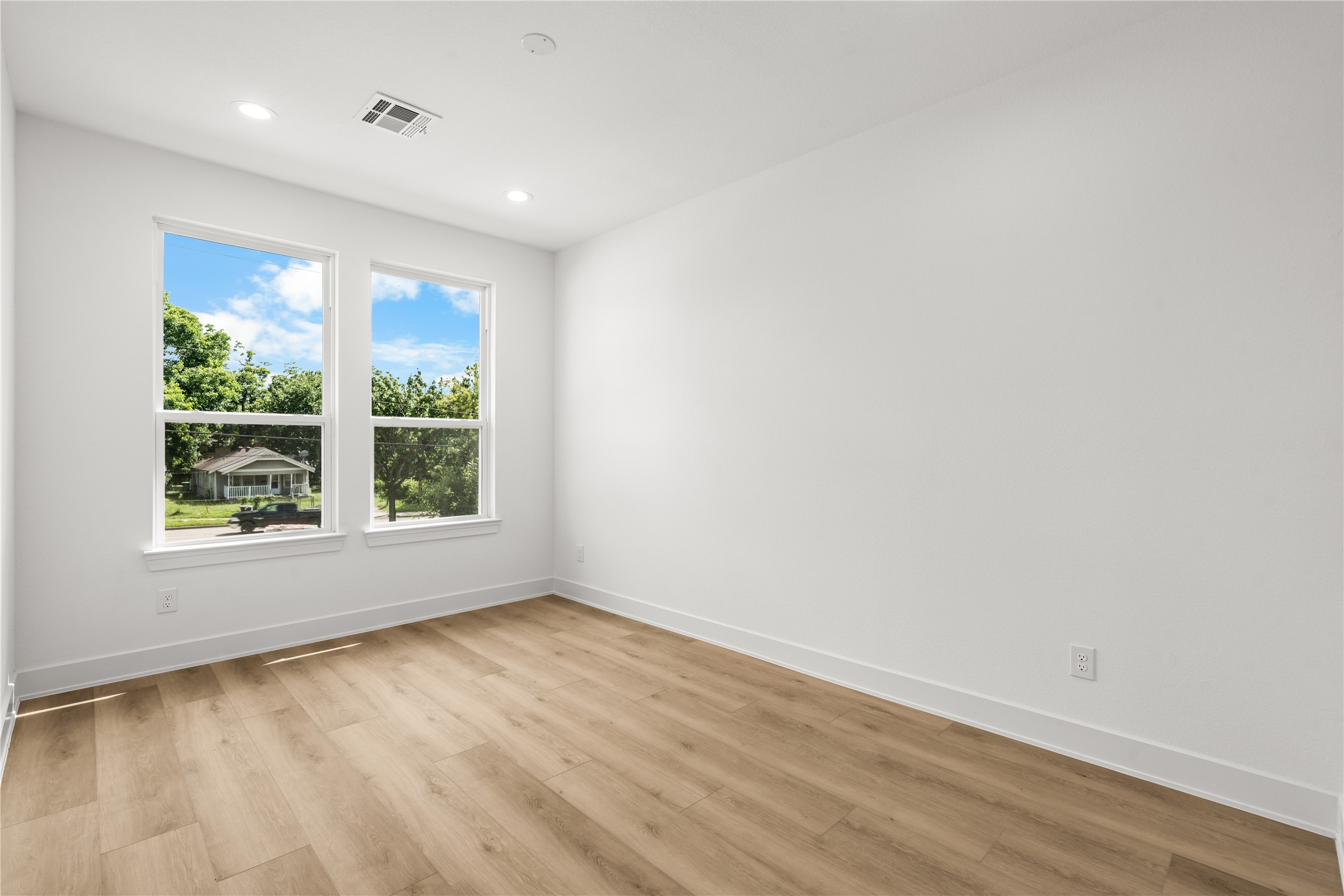 The third bedroom features LVP flooring, smooth white walls, and two large windows with views of mature trees and greenery. The bright, peaceful layout works perfectly as either a bedroom or a home office.