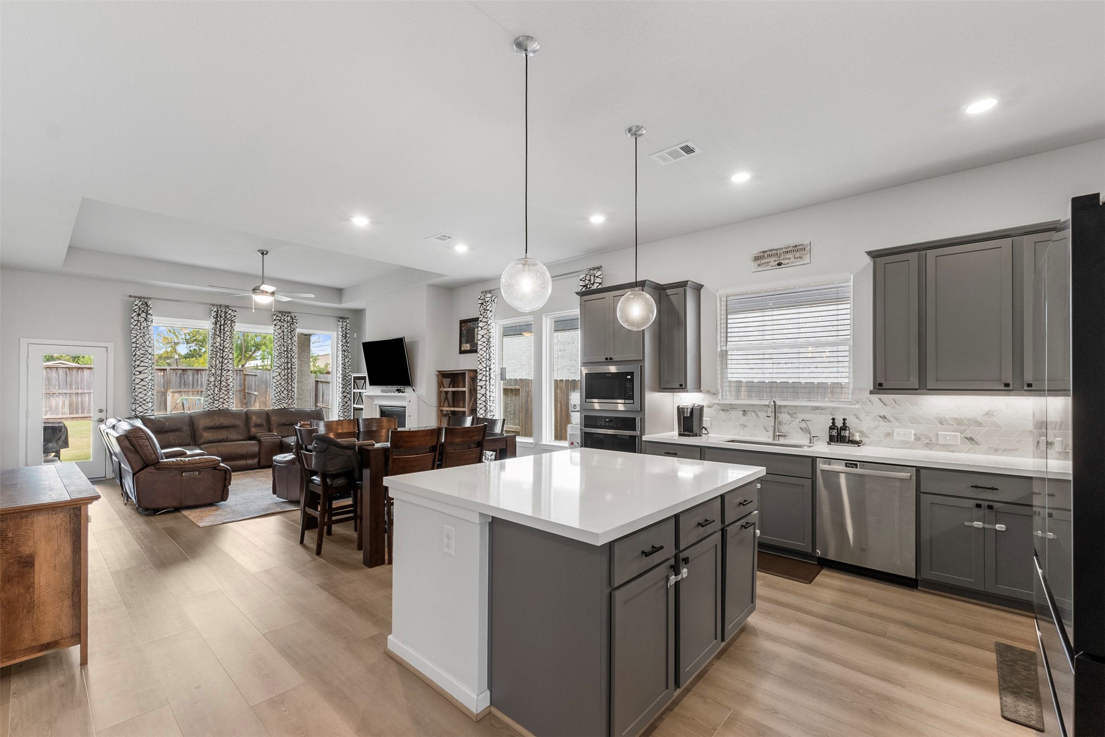 Spacious open-concept kitchen and living area featuring a large island with modern pendant lighting, sleek gray cabinetry, and stainless steel appliances.