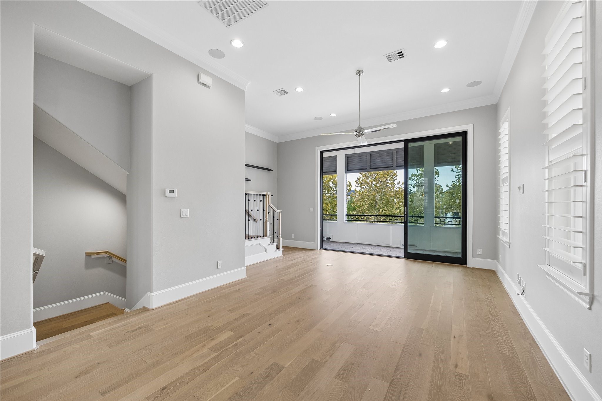 Bright and spacious living area with sleek hardwood floors, recessed lighting, and large sliding glass doors leading to a balcony with harmonious views of water, perfect for indoor-outdoor living.