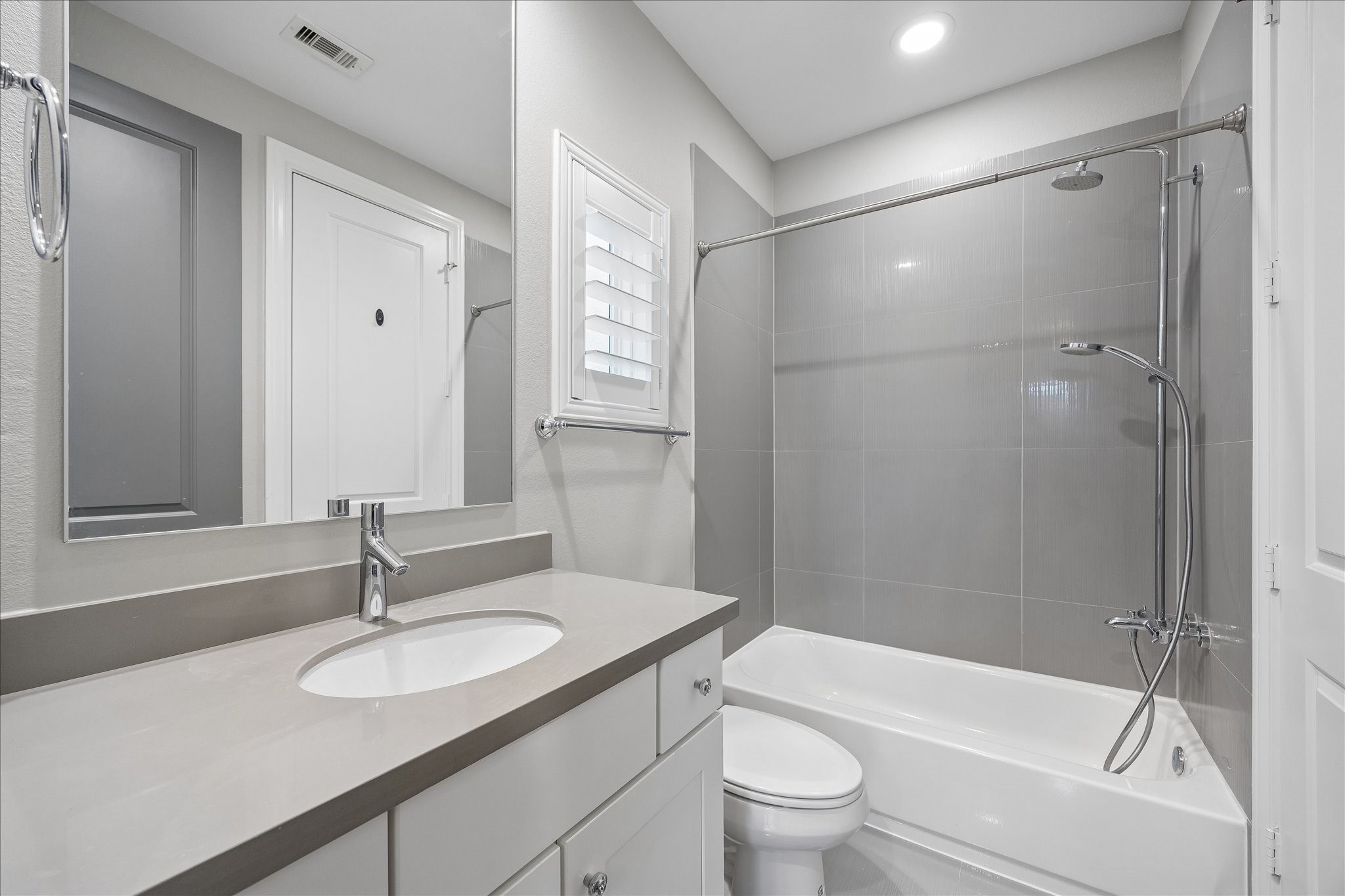 En-suite bath in first floor bedroom. Modern bathroom featuring sleek gray tiles, a spacious vanity with an undermount sink, and a pristine bathtub-shower combo, complemented by soft lighting for a clean and inviting atmosphere.