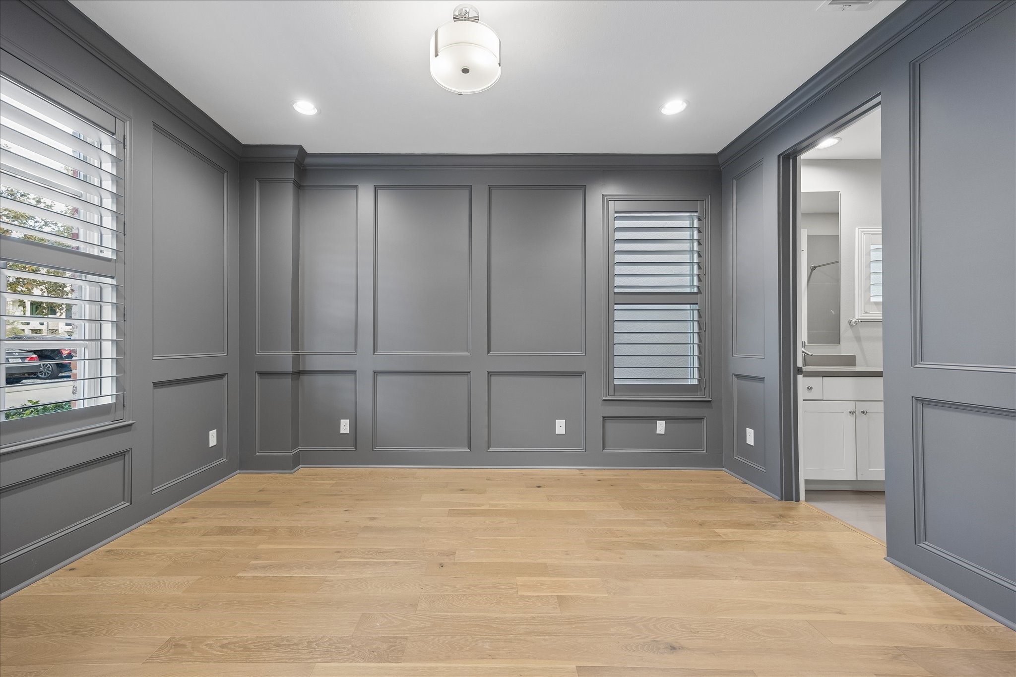 Elegant room with rich gray paneled walls, hardwood floors, and stylish plantation shutters, offering a modern and sophisticated ambiance.