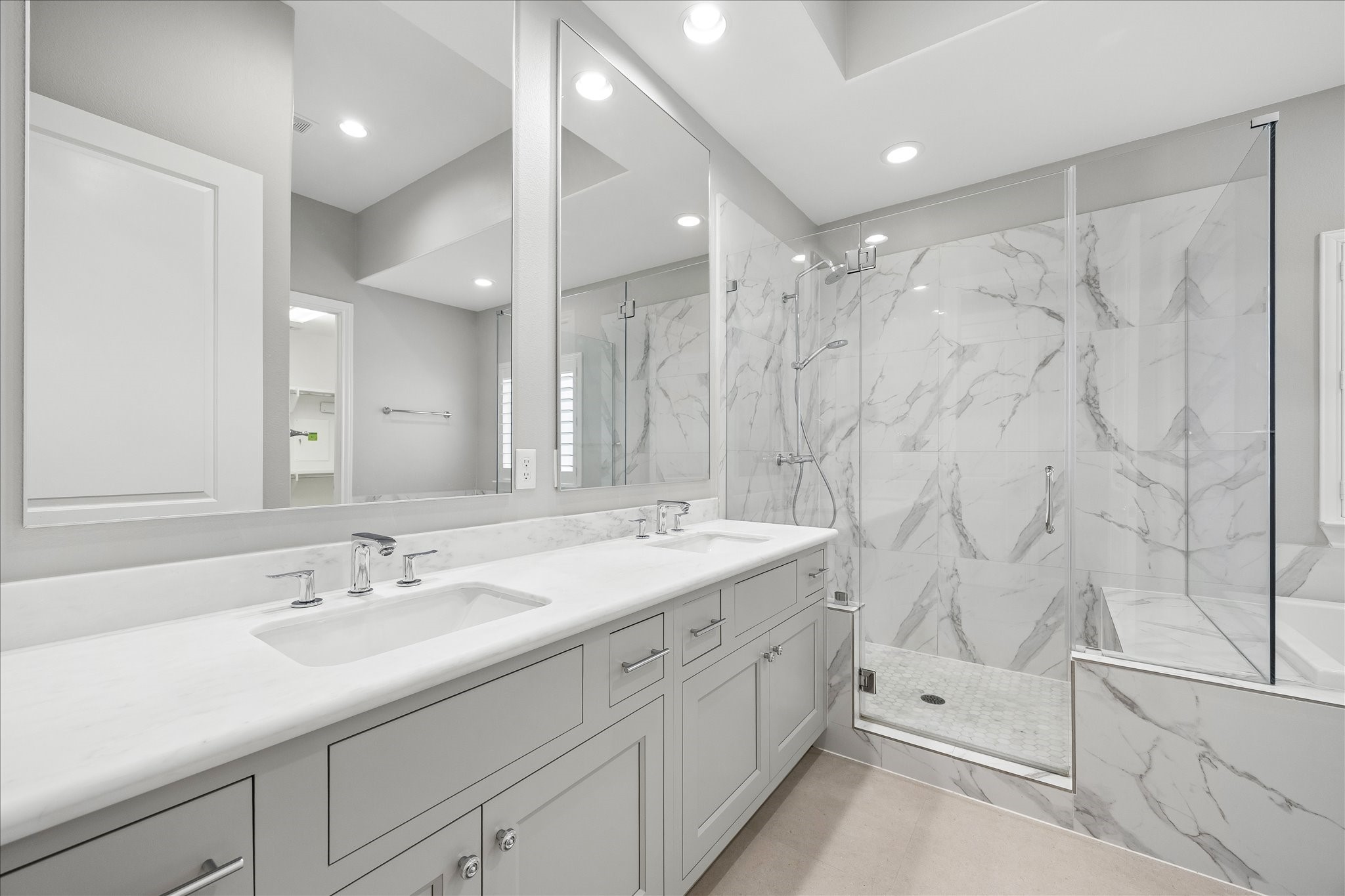 Elegant bathroom featuring a spacious double vanity with modern fixtures, a sleek glass-enclosed shower, and luxurious marble tile accents.