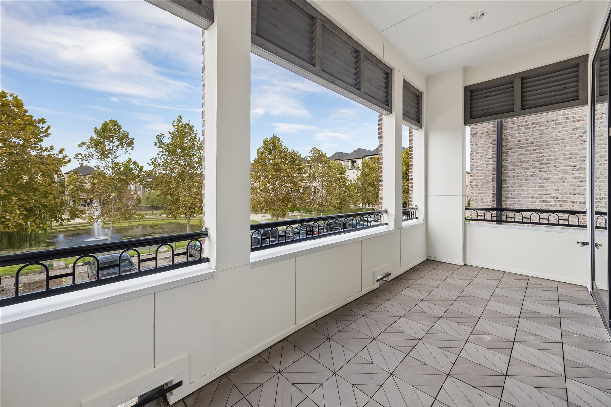 Spacious covered balcony with elegant tile flooring offers scenic views of mature trees and a serene fountain, perfect for relaxation and outdoor enjoyment. Large enough for table, chairs, and entertainment with great views.