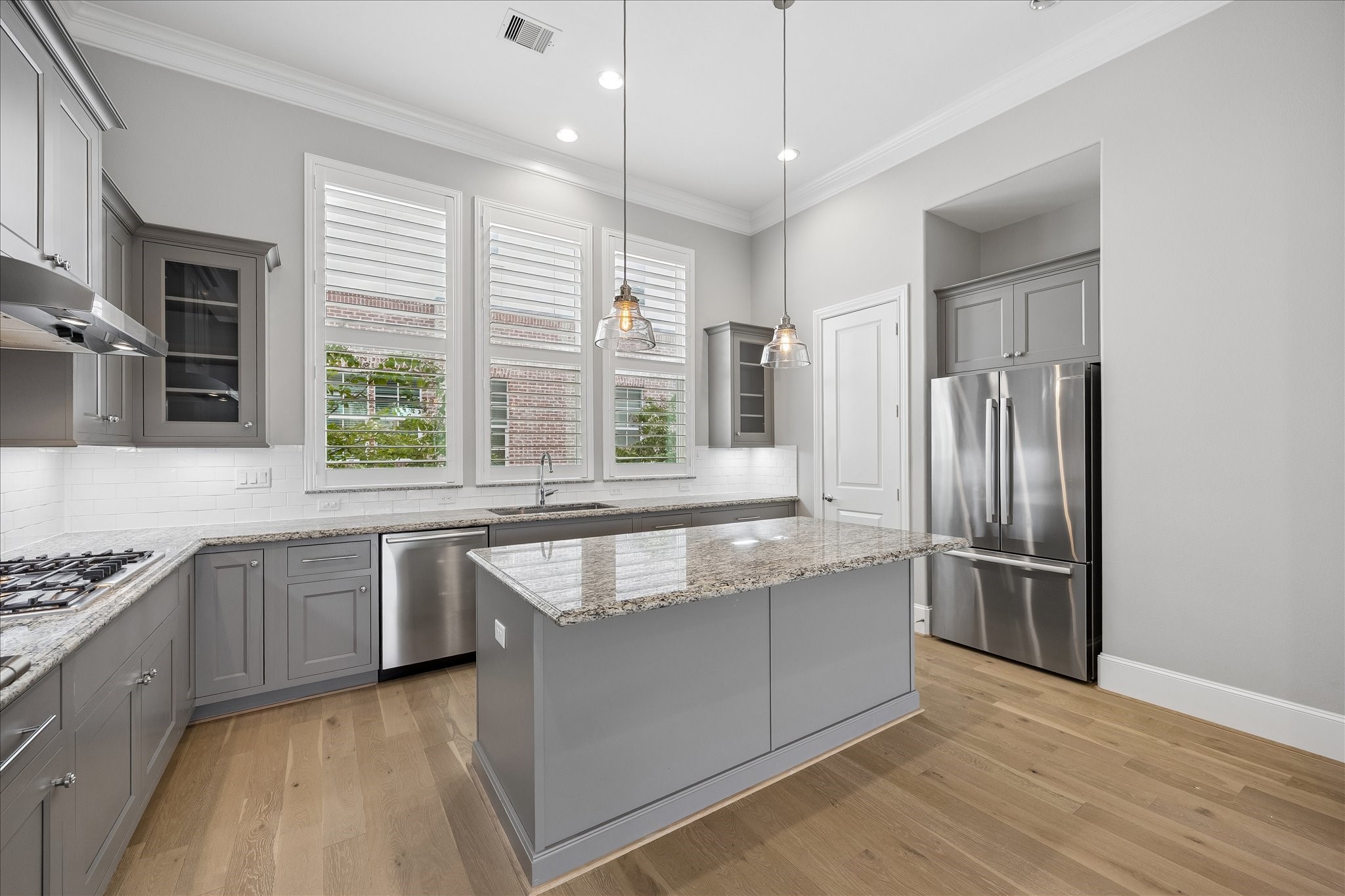 Modern kitchen with sleek gray cabinetry, a spacious granite-topped island, and stainless steel appliances. Open to living area and walk-in pantry. Refrigerator included.