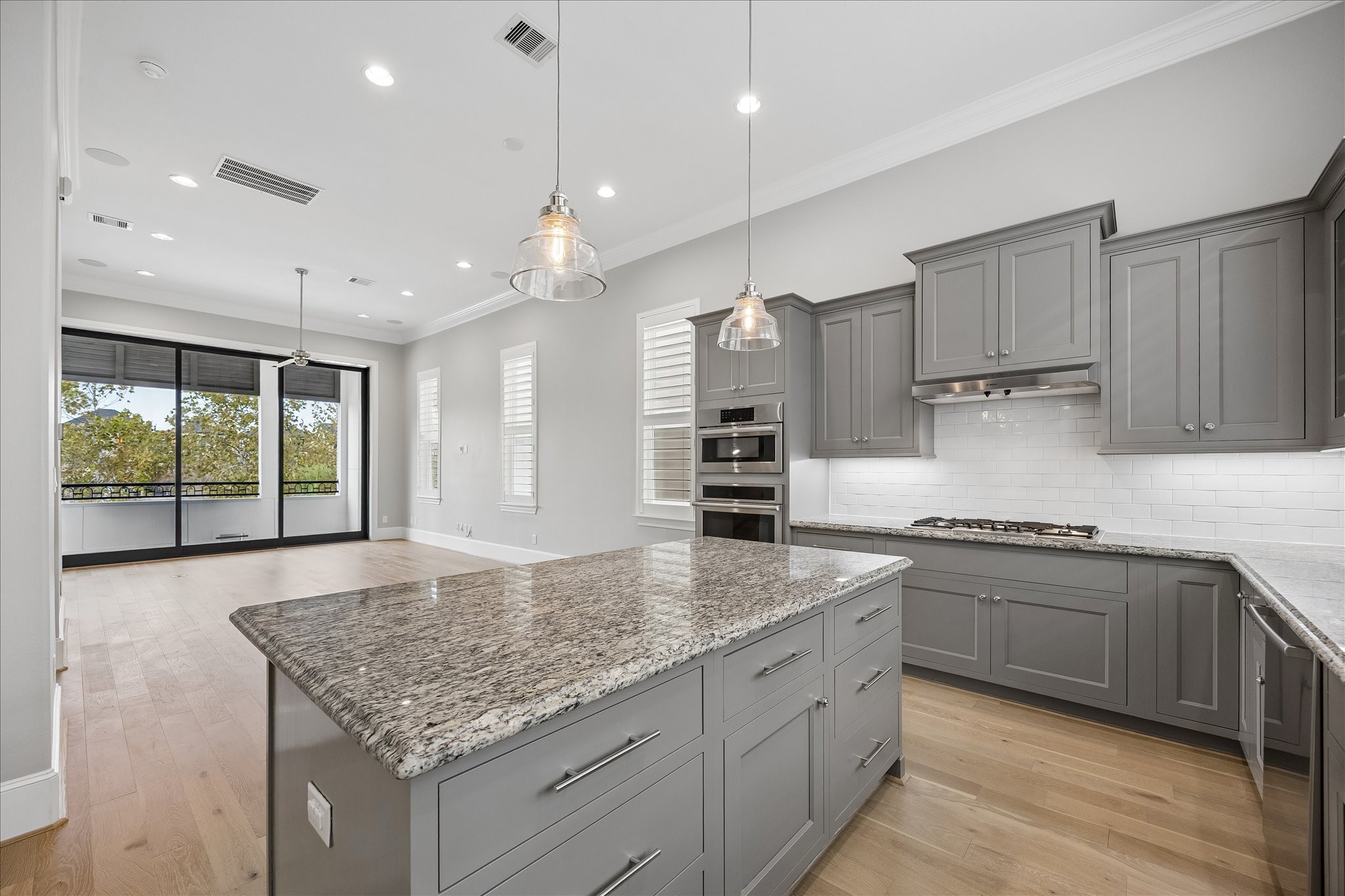 Spacious modern kitchen with sleek gray cabinetry, granite countertops, and stainless steel appliances, opening to a bright living area overlooking the Lake with fountain view and large windows and hardwood floors.